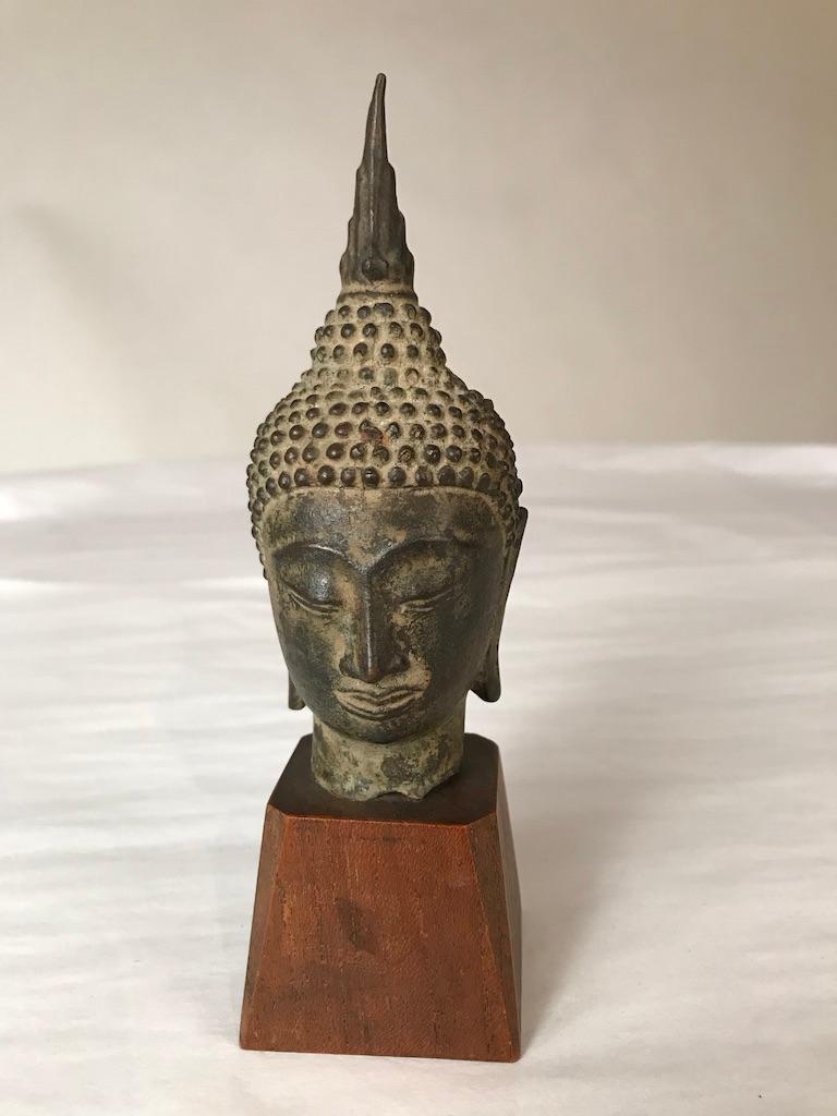 A Thai, Ayutthaya style, bronze head of Buddha Shakyamuni, late 16th or early 17th century. With a serene expression on his face, downcast eyes, arched eyebrows, smiling lips, with curled headdress and ushnisha topped by a flame. 
Measures: 6.75