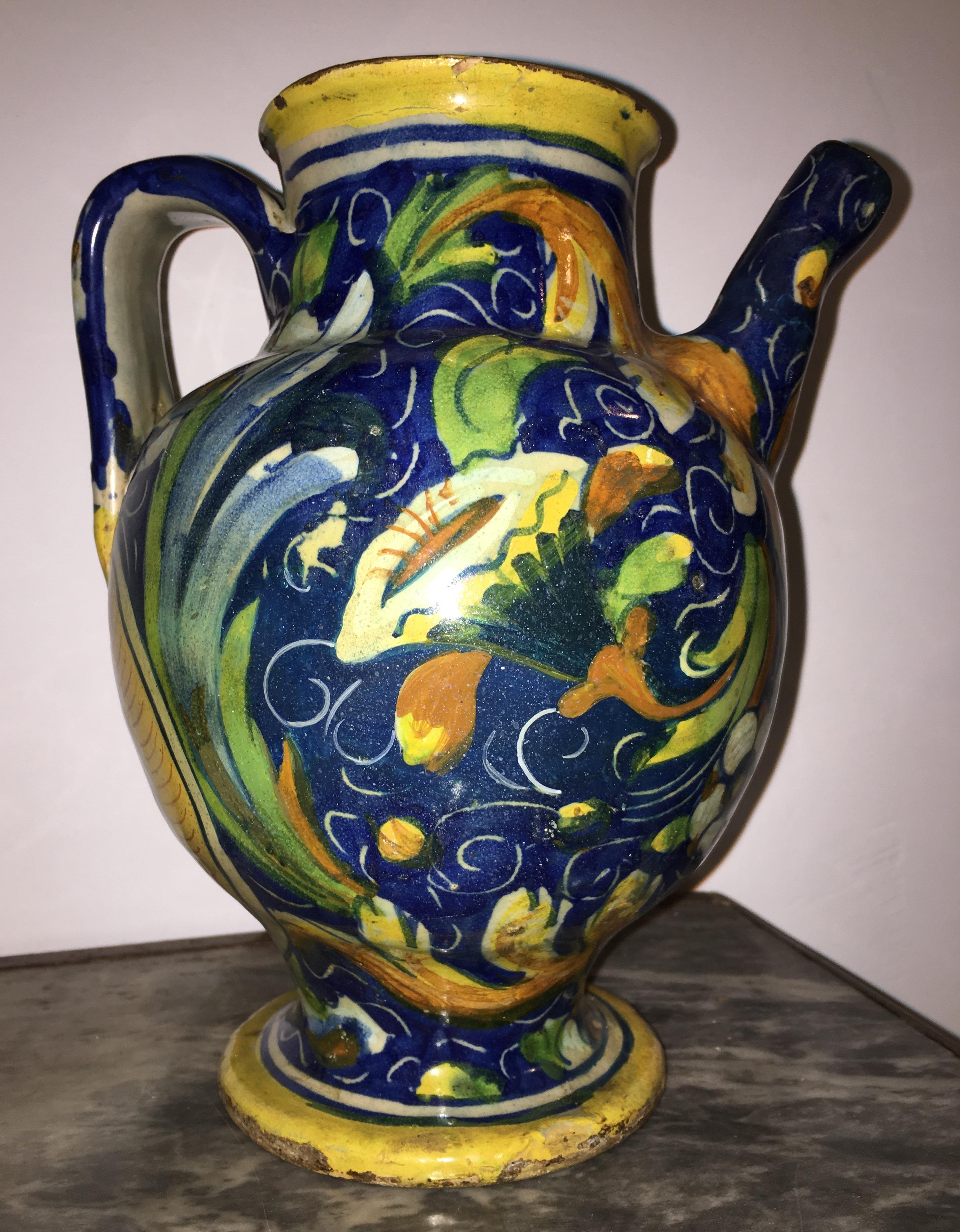 18th century Venezia Maiolica jug within the medallion placed in the back of the jug with the figure of a saint. All around there is the decoration of flowers, fruit trees and leafy branches, as well as curls made from scratch on the blue background.