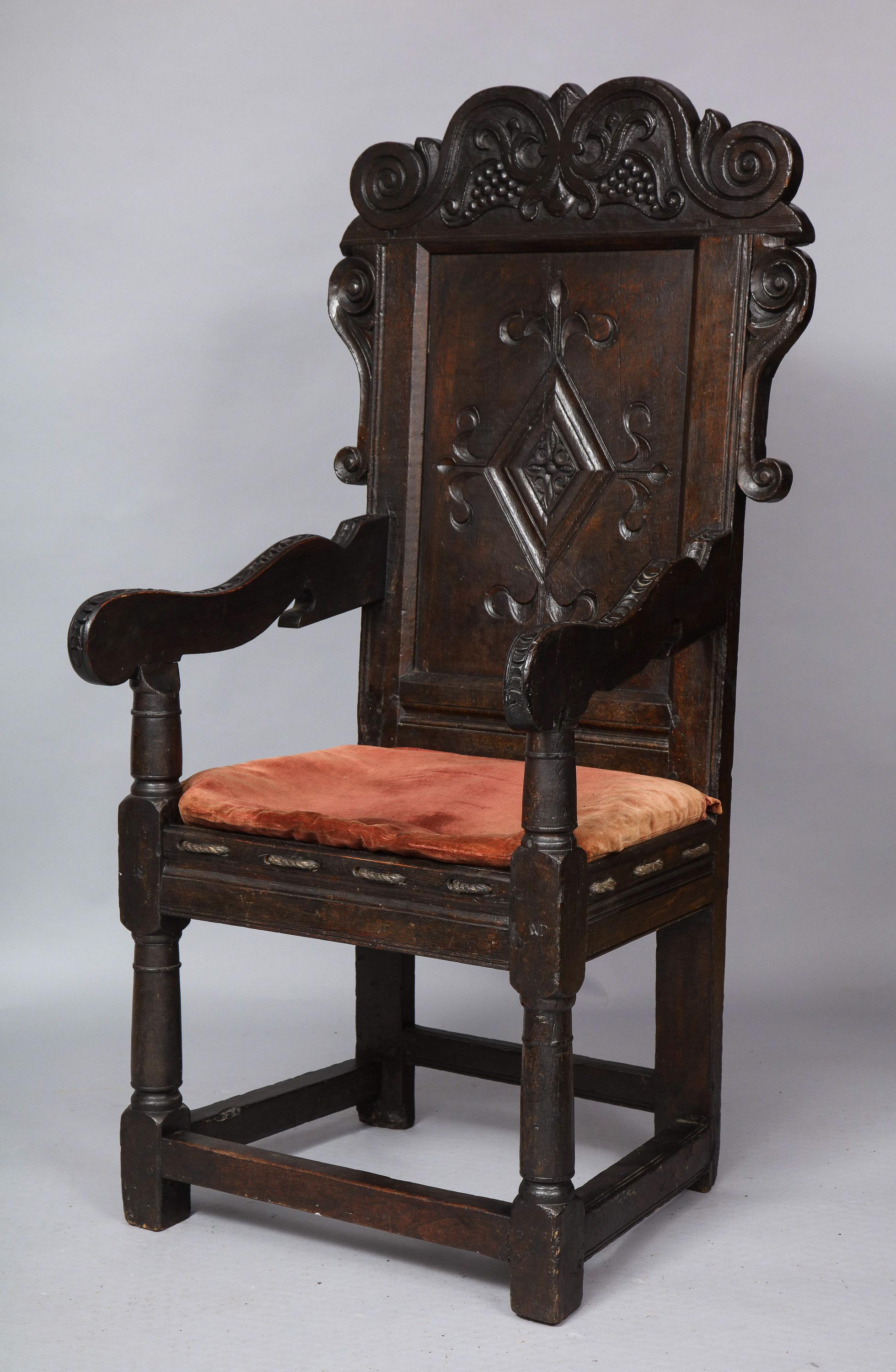 Fine English 17th century oak wainscot chair, the scroll and strapwork decorated crest with carved berries, over diamond carved back panel, the shaped arms over woven rope cushion support and standing on cannon barrel turned legs joined by box