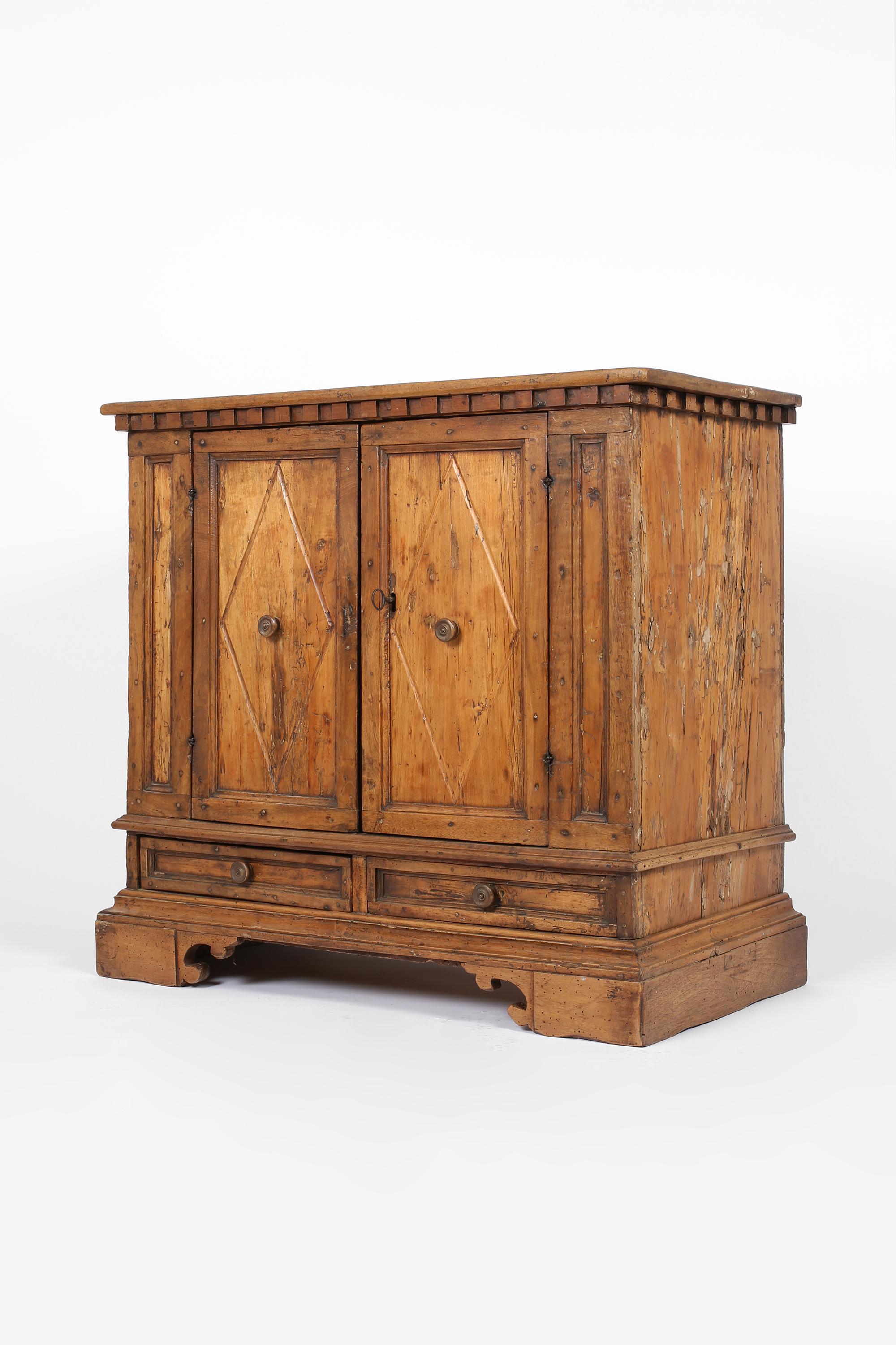 A 17th century heavily patinated walnut cabinet/credenza from Florence. Featuring a typical crenellated frieze and decorative moulding/fretwork - the two geometric panelled doors open to reveal a single internal shelf with two drawers below. Highly