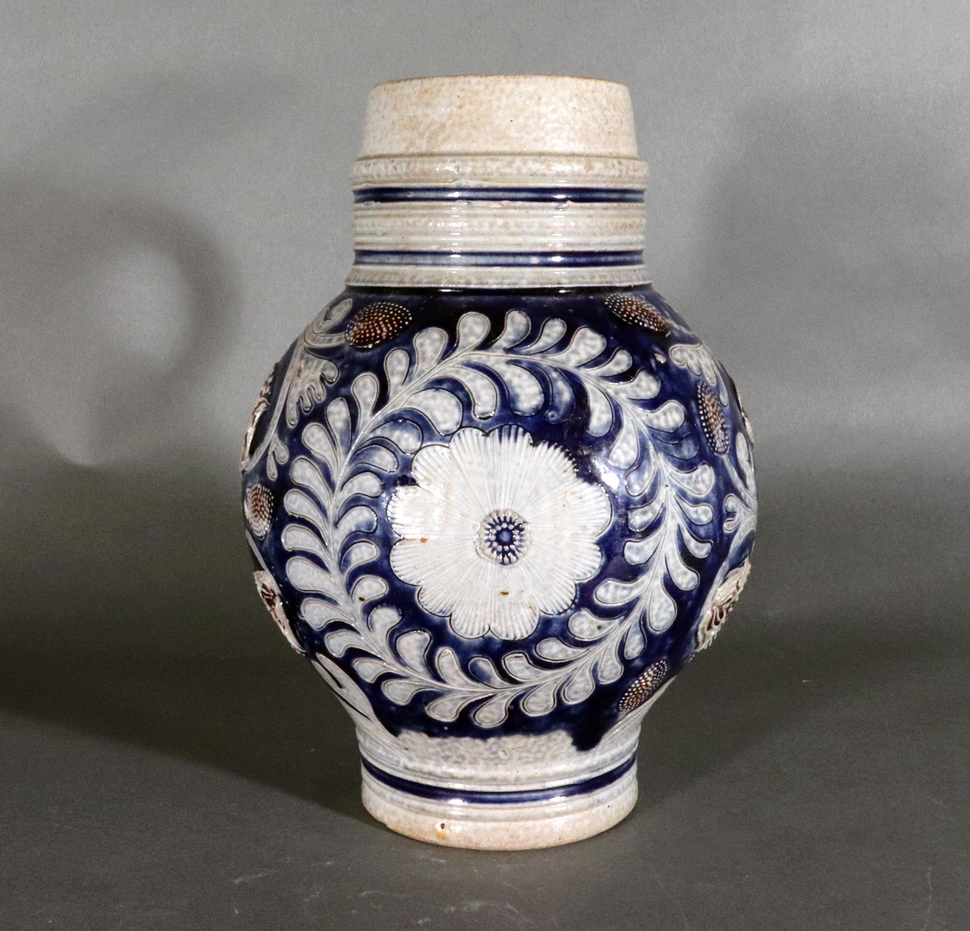 Westerwald Blue & Manganese Stoneware Jug,
17th Century

The blue and gray jug molded with incised scrolling flower stems and molded flower heads.  There is a central flower head roundel with a molded leaf surround.  To each side are similar designs