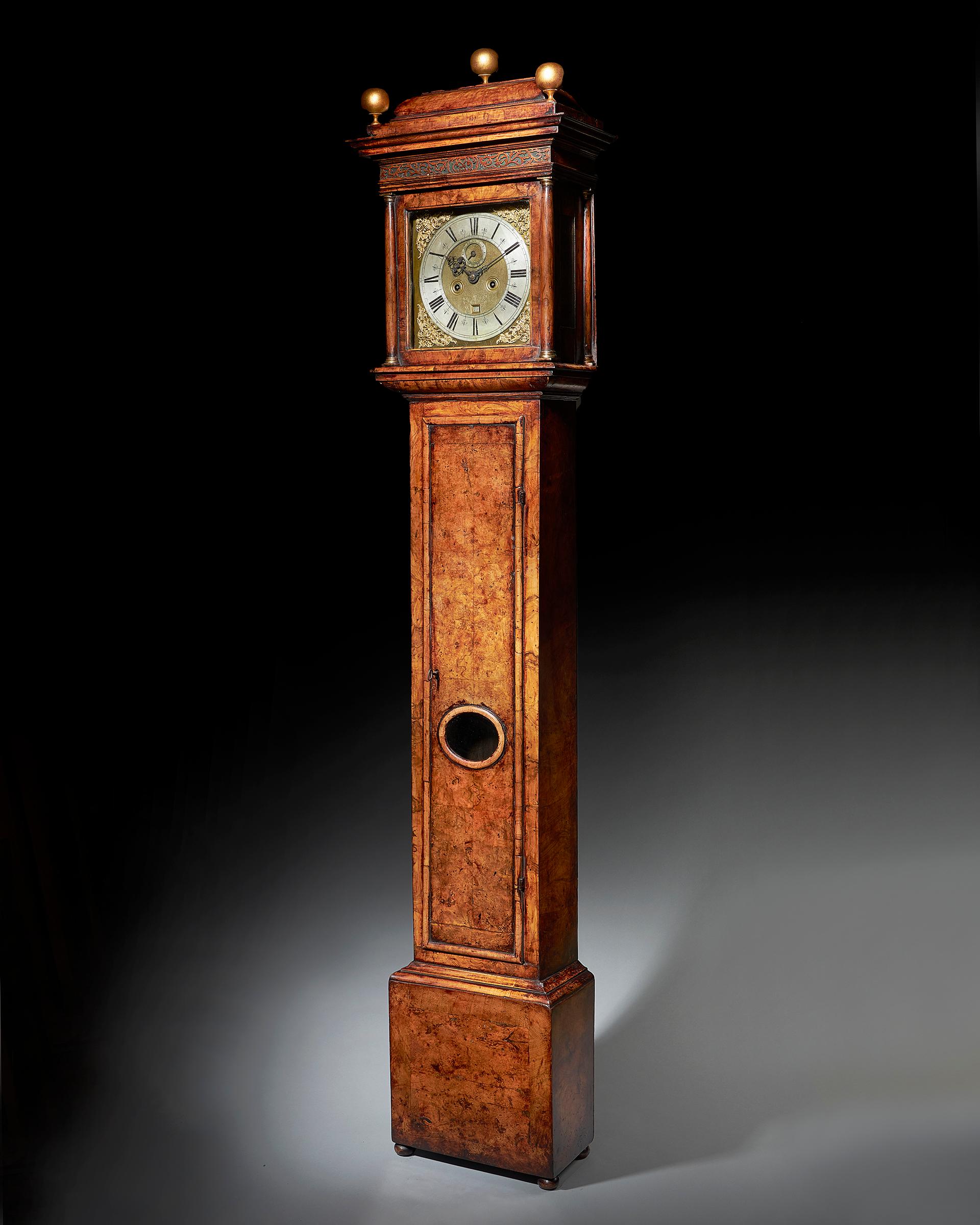 The attractive burr walnut-veneered oak case is of classic design for the period and has a warm patina. The formerly rising hood has a shallow caddy, lovely blind fretwork in the frieze, is flanked by plain brass-capped columns and has glazed