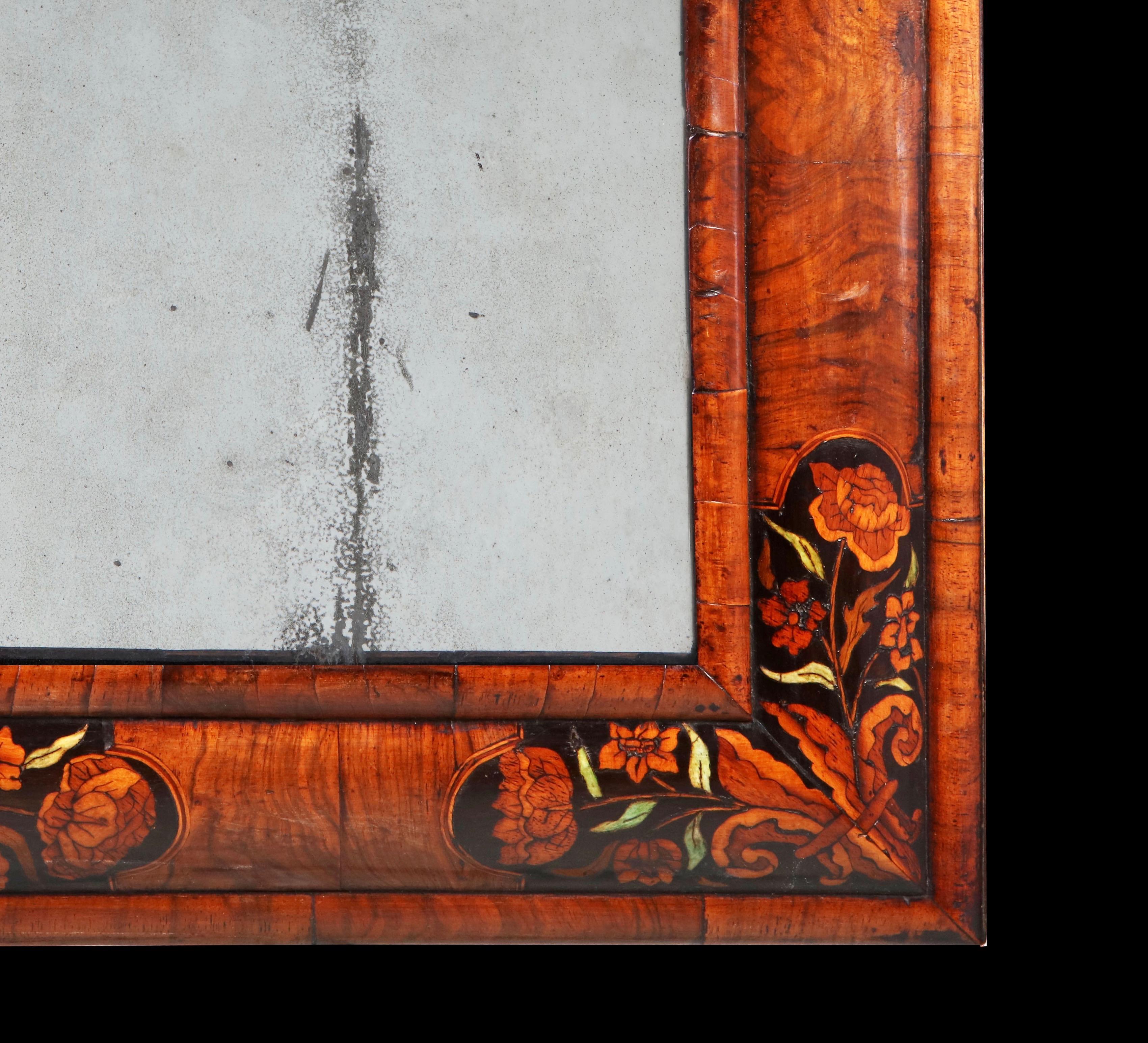From the restoration of the British Monarchy (1670-1685) we bring to you this charming walnut and marquetry cushion mirror depicting spring flowers and scrolling fleur-de-lis inside ebony and box strung break-arch reserves, on an ebony