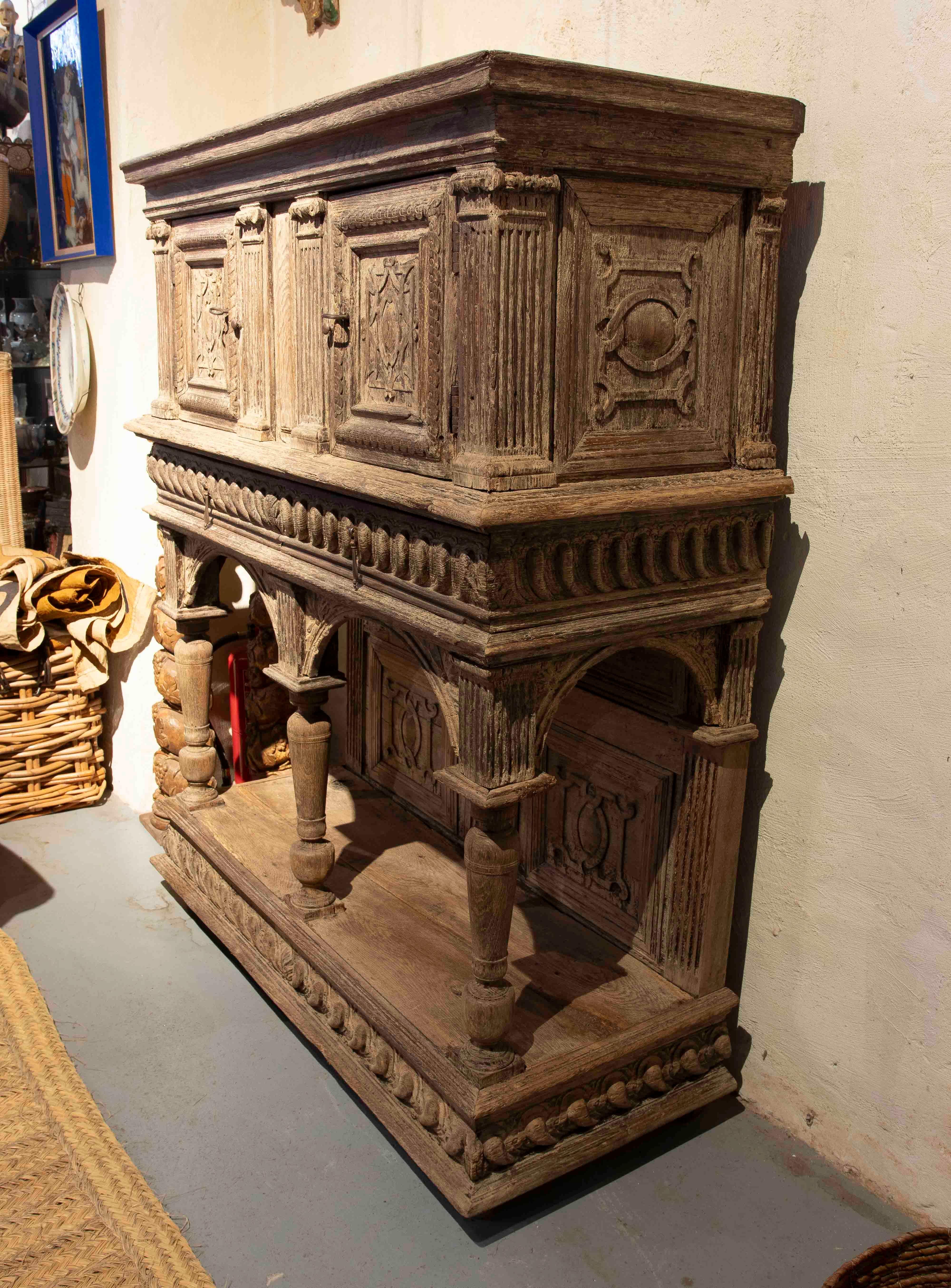 Majestic buffet en bois massif avec un impressionnant travail de sculpture à la main. Sa structure robuste et détaillée évoque l'élégance des meubles de la Renaissance, avec des colonnes tournées, des reliefs géométriques et des portes décorées de