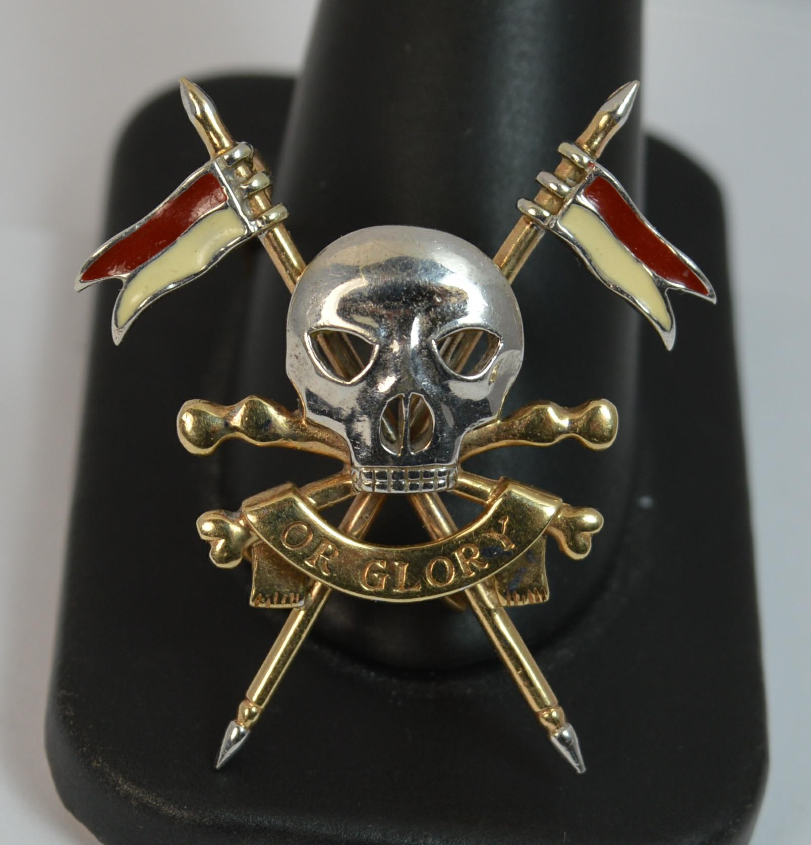 
A great quality skull brooch.

Solid 9 carat yellow gold brooch with a large skull to the centre in white gold. 

The large skull is to the forefront with bones below and a banner to read Or Glory. The background is of a spear flag of red and cream