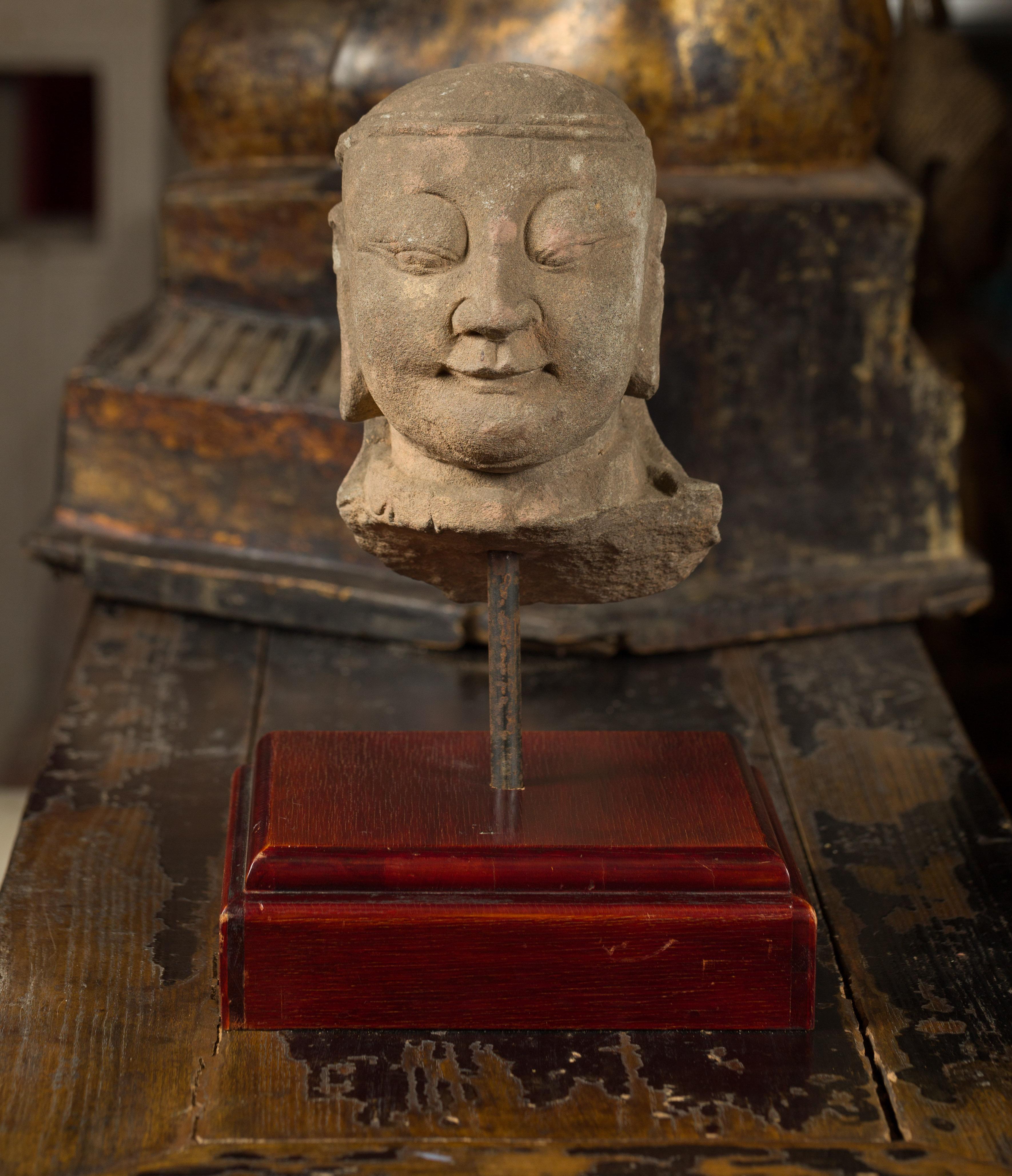 A Burmese hand carved stone sculpture from the 17th or 18th century, depicting a man's head and mounted on a custom wooden base. Hand carved from stone in Burma during the 17th or 18th century, this sculpture, featuring a man's head and showcasing a