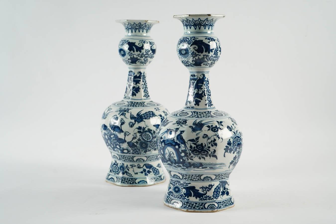Pair of large faience bottled vases. Orthogonal base, round body with a narrow neck ended by an open bulb.
Hand-painted in Delft blue shades the ornamentation consists of a blossoming landscape with lotus, tulips and chrysanthemums among waters and