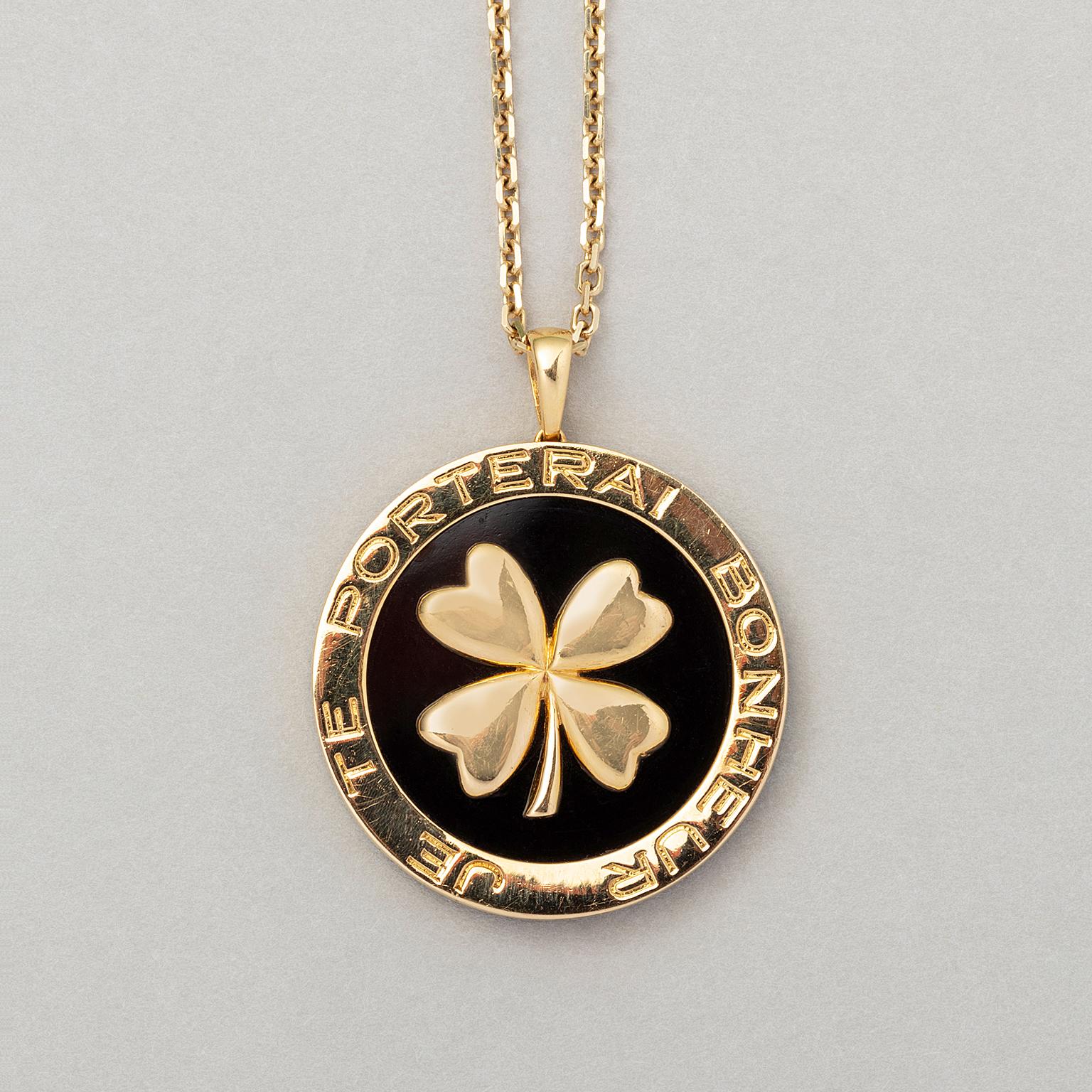 An 18 carat yellow gold round pendant with a lucky four-leaf clover set on black agate. On the border it says 'je te porterai bonheur' which means 'I will bring you happiness'. Signed and numbered: Van Cleef & Arpels, B1298X5. The pendant includes a