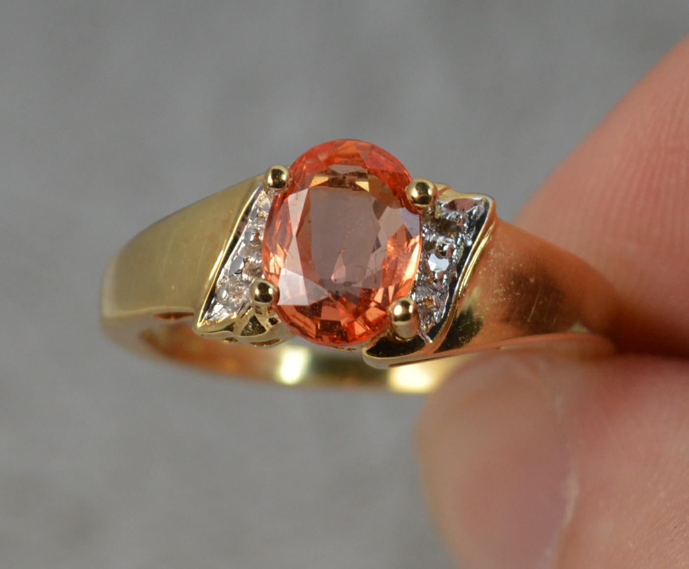 A superb 18ct Gold, Sapphire and Diamond ring. 
Designed with an oval cut vivid peachy orange coloured sapphire in four claw setting. 12.7mm x 5.6mm approx. Padparadscha sapphire. A small diamond to each side.
Solid 18 carat yellow gold example.