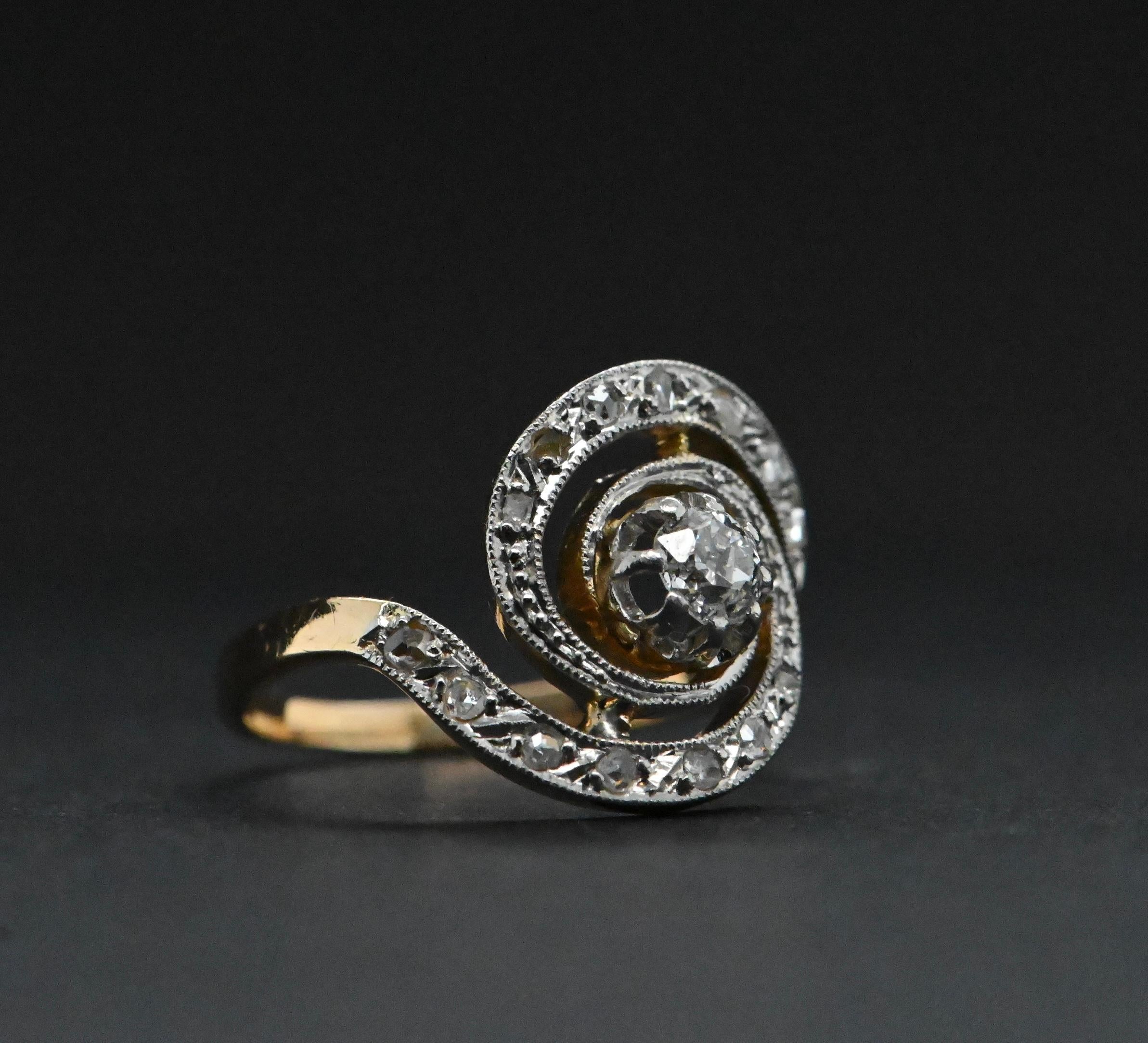 Cette somptueuse bague en or jaune 18 carats, datant de 1925, est un véritable trésor d'époque. Il est orné de diamants totalisant plus d'un carat, ce qui lui confère une brillance exceptionnelle. Le design en forme de tourbillon est magnifiquement