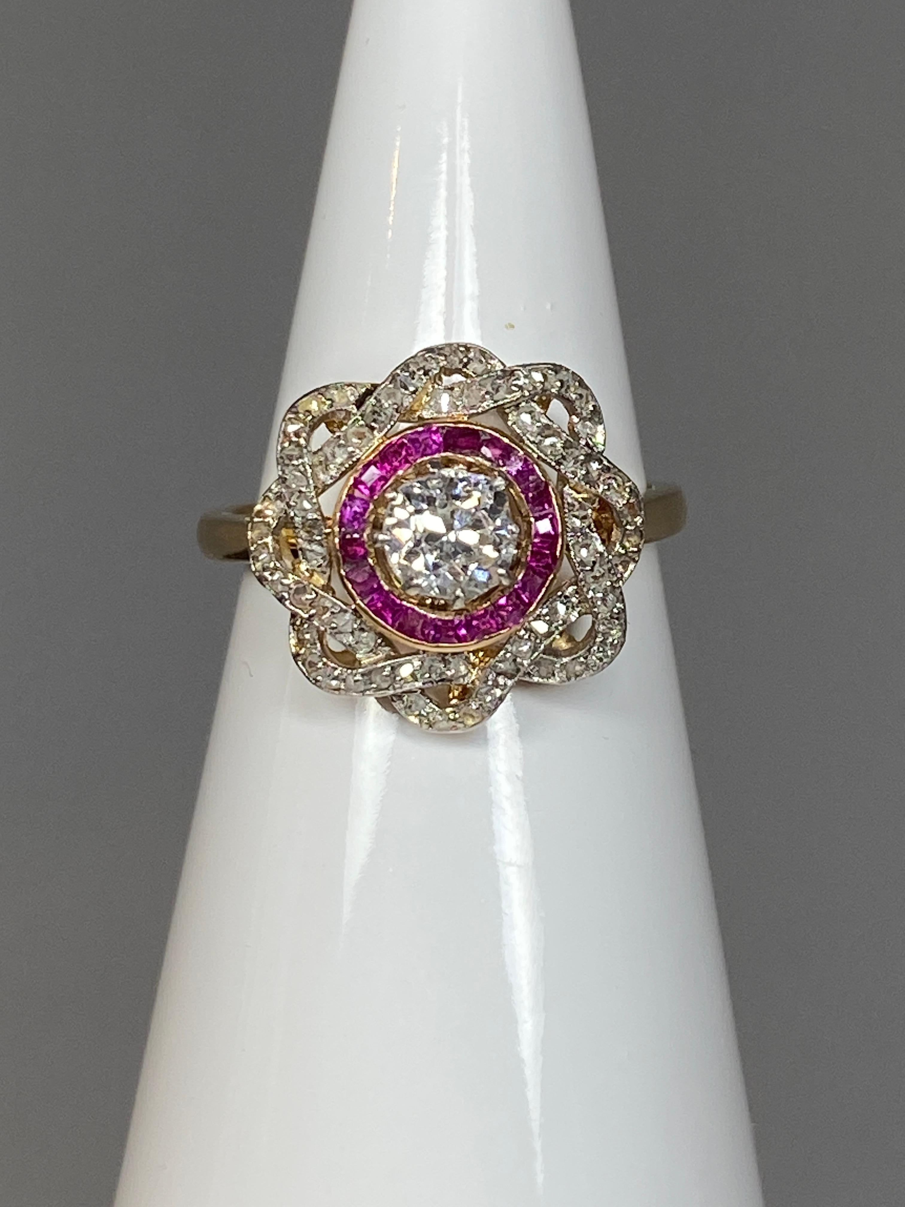 Ravissante bague en or 18 carats ornée au centre d’un diamant de taille ancienne pesant 0.30/0.40 carat environ, entouré d’une ligne de rubis calibrés et de 2 lignes entrelacées serties de petits diamants taillés en rose. Le diamant surélevé est en