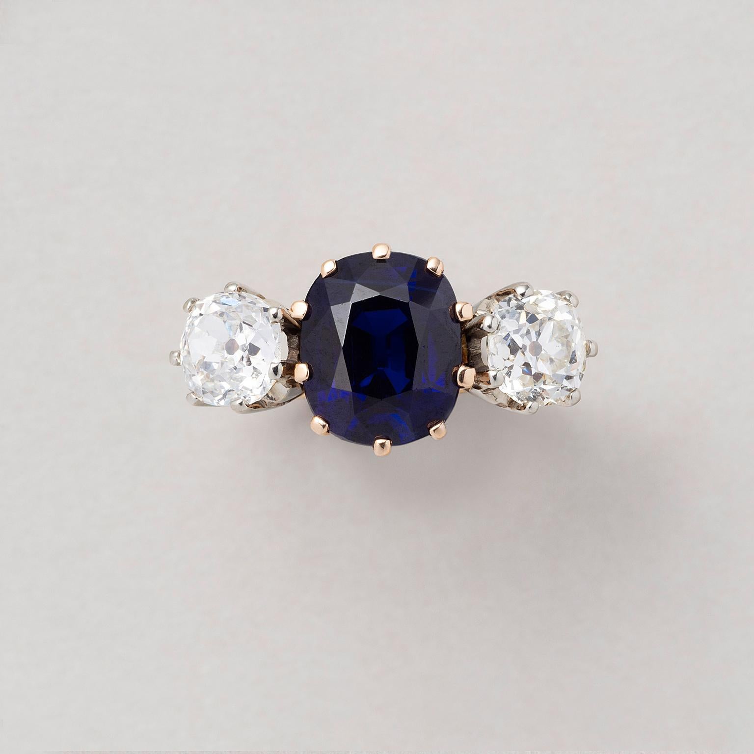  An 18 carat yellow and white gold three stone ring with a natural unenhanced cushion cut blue sapphire (3.91 carat, basaltic origin) with on each side a cushion cut diamond (each app. 0.85 carat, I, Vs-Si), Swiss.

Period: 1950-1960-1970
Ring size: