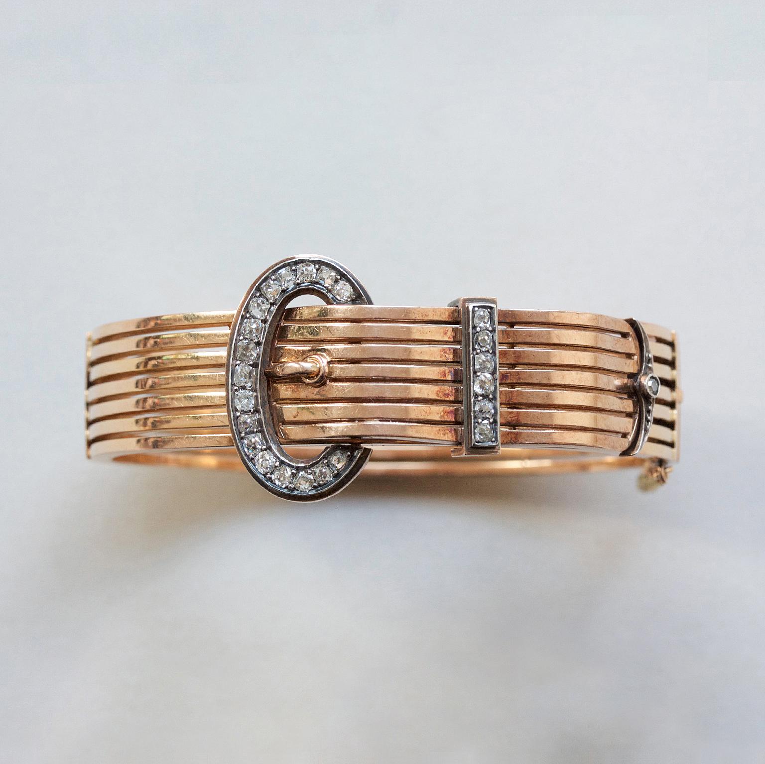 An 18 carat rosé gold bangle with horizontal stripes in the shape of a buckle set with old cut diamonds on the buckle, France, master mark: E crown W, 19th century.

weight: 40.77 gram
width: 2.4 - 1.4 cm
dimensions: 5.9 x 5.6 cm fits a normal size
