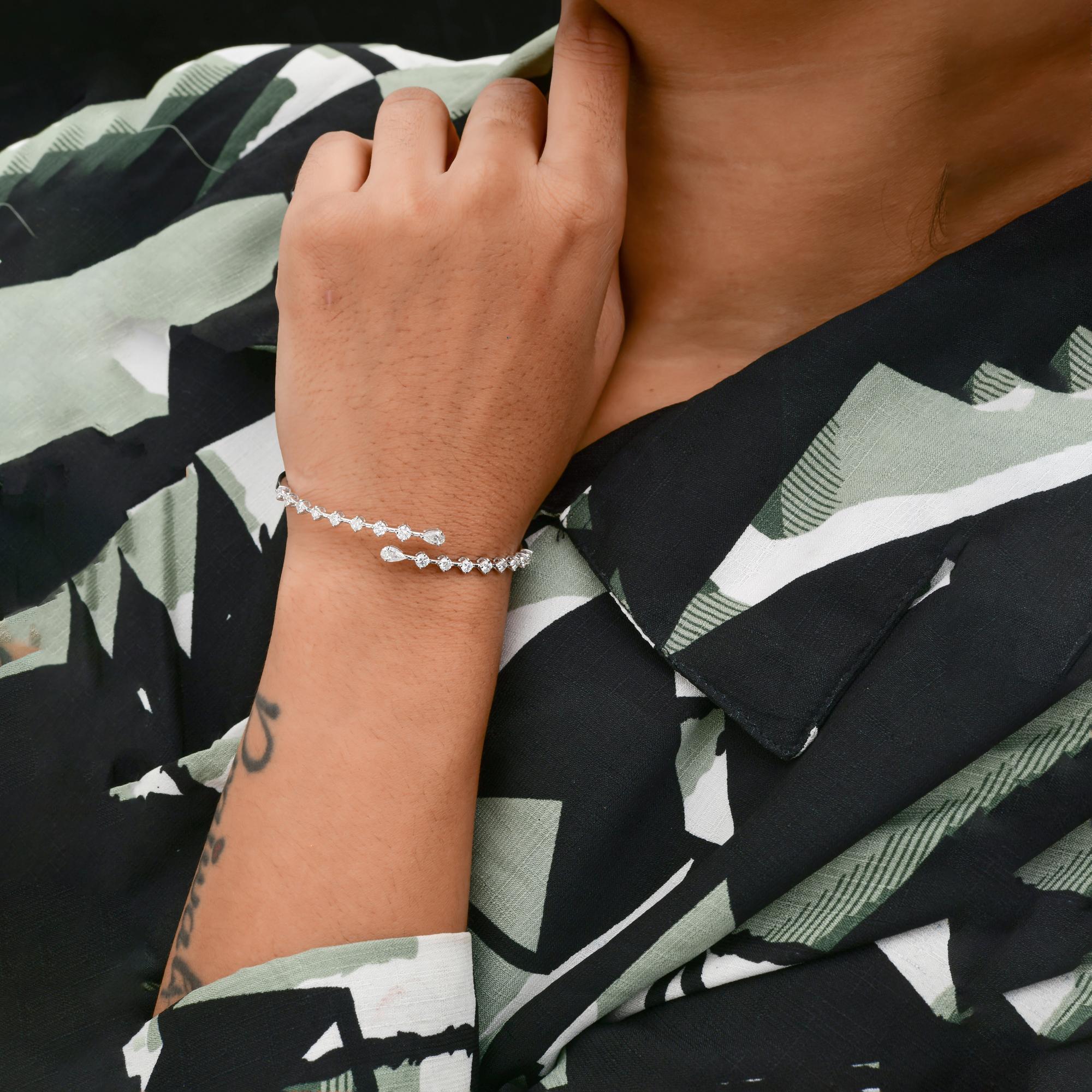 Esta pulsera brazalete de oro blanco de 18 quilates con diamantes talla redonda de 1,8 quilates, claridad SI y color HI, tiene diamantes talla pera en cada uno de los extremos abiertos de la pulsera, cerrados con un mecanismo de cierre. 
Los