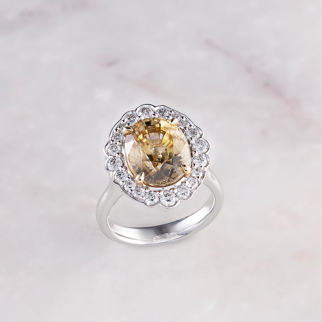 Matthew Ely 18ct white gold cocktail ring with yellow gold claws. Set with 1 = 9.75ct oval cut gold zircon + 8 = 0.216ct round diamonds. With a 9.75ct Oval Cut Gold Zircon at its center, this ring is surrounded by 0.216ct Round Brilliant Cut