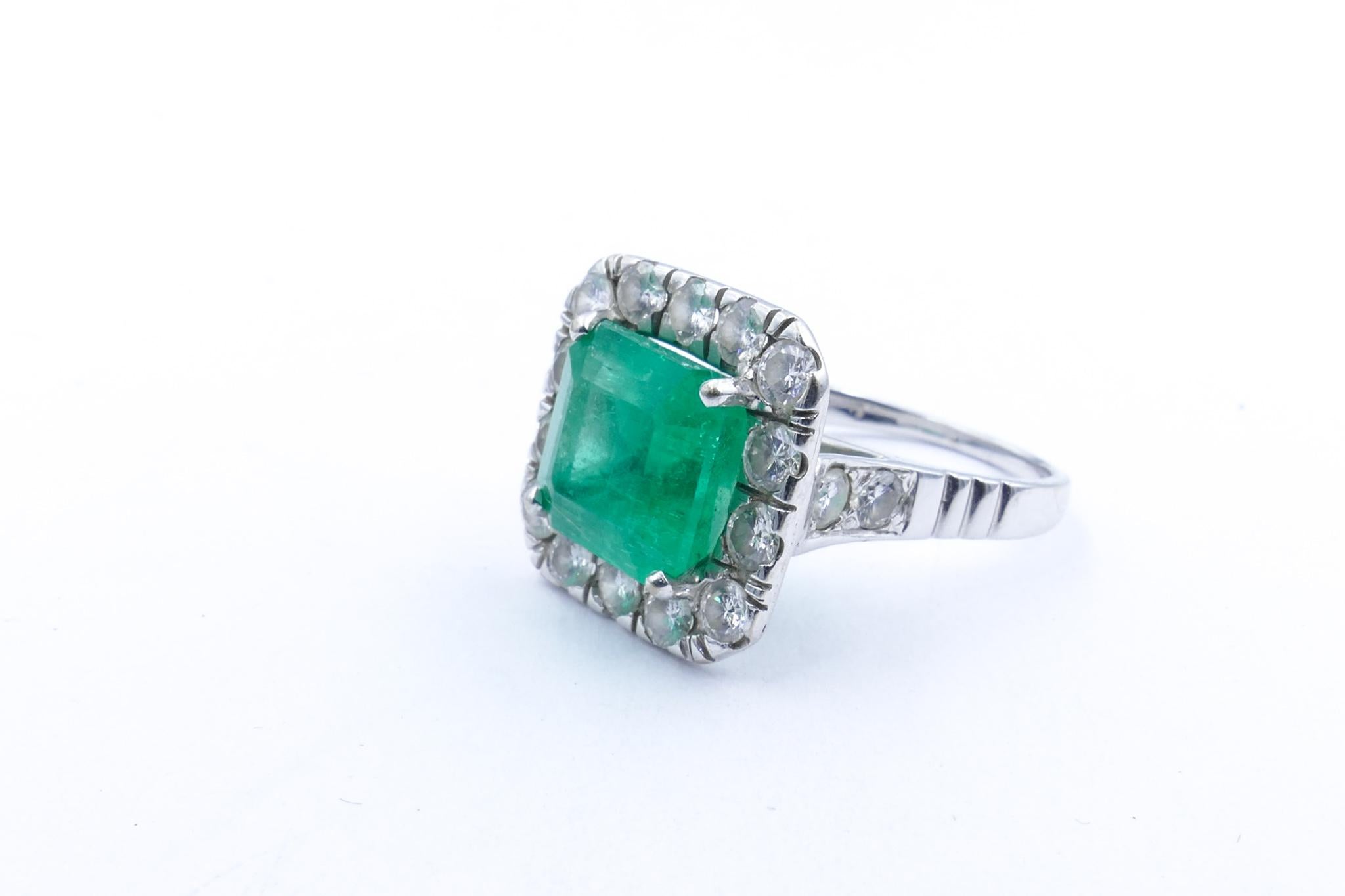 Of a gorgeous mid bluish- green Colour this fine Square Emerald Stone of 5.23 carats, measuring 10.26mm X 10.09mm X 7.07mm is the Centrepiece of  this outstanding Ring & is surrounded by 18 Round Brilliant Cut Diamonds, Bead Set,
Colour G/H &