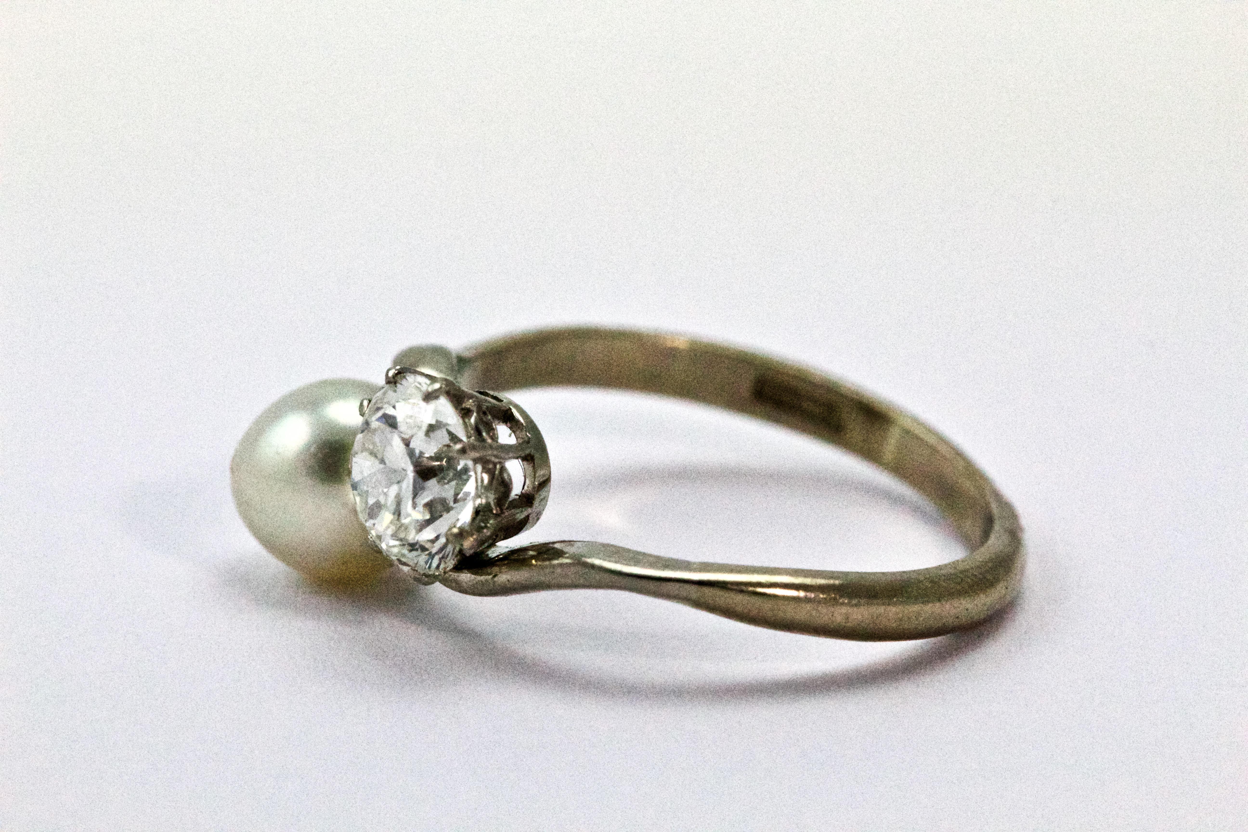 This elegant Edwardian ring features an Old European cut diamond claw set and a natural pearl. The diamond is certified 1.02 ct with colour H and clarity VS1. The pearl and the diamond are set in 18 carat white gold in a crossover design, also