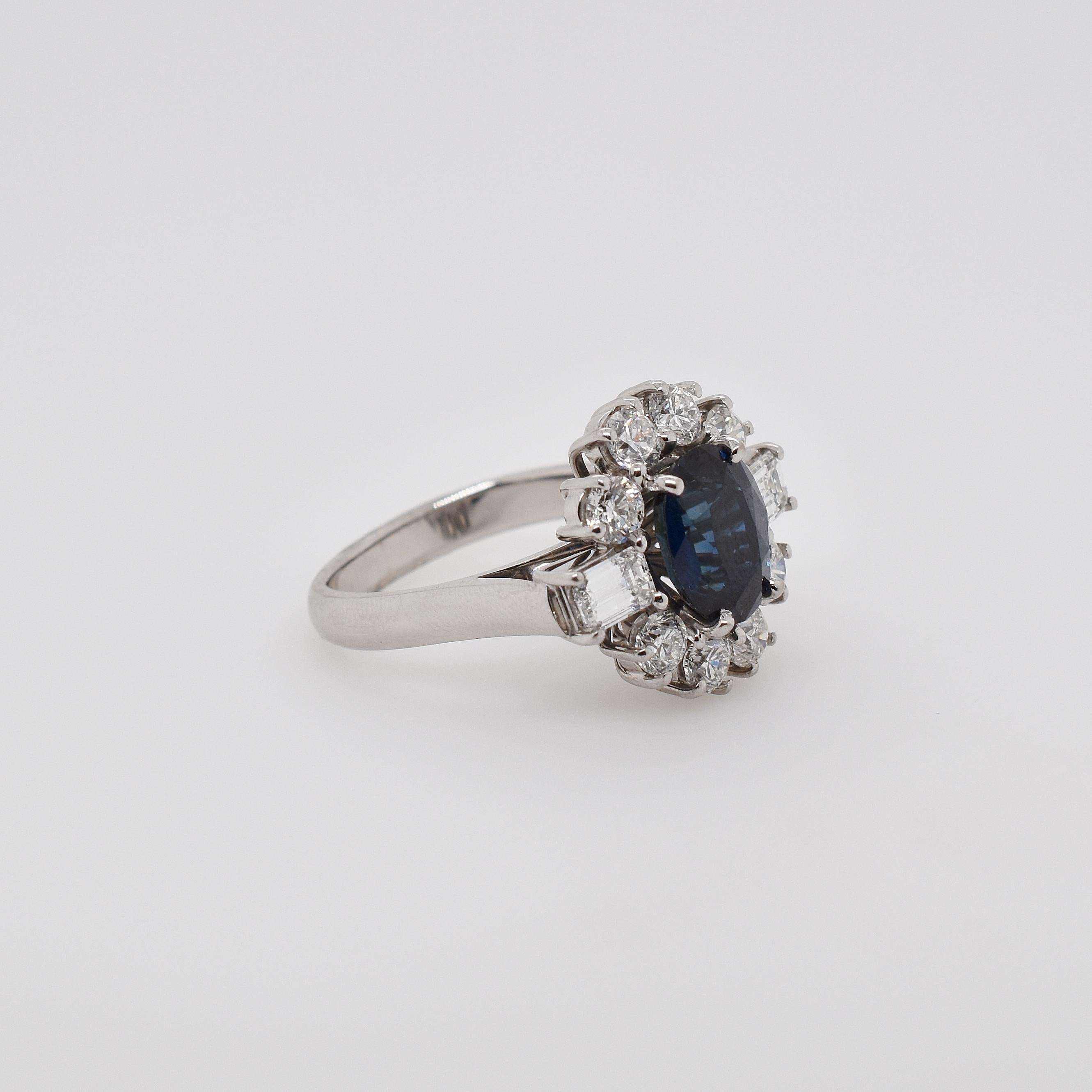 18ct white gold Reddestone creek sapphire and diamond cluster ring. The oval sapphire is 3.88ct, surrounded by round brilliant and emerald cut diamonds. 2 emerald cut totalling 0.67ct and 8 round brilliant totalling 1.45ct. US size 6 1/2 - can be