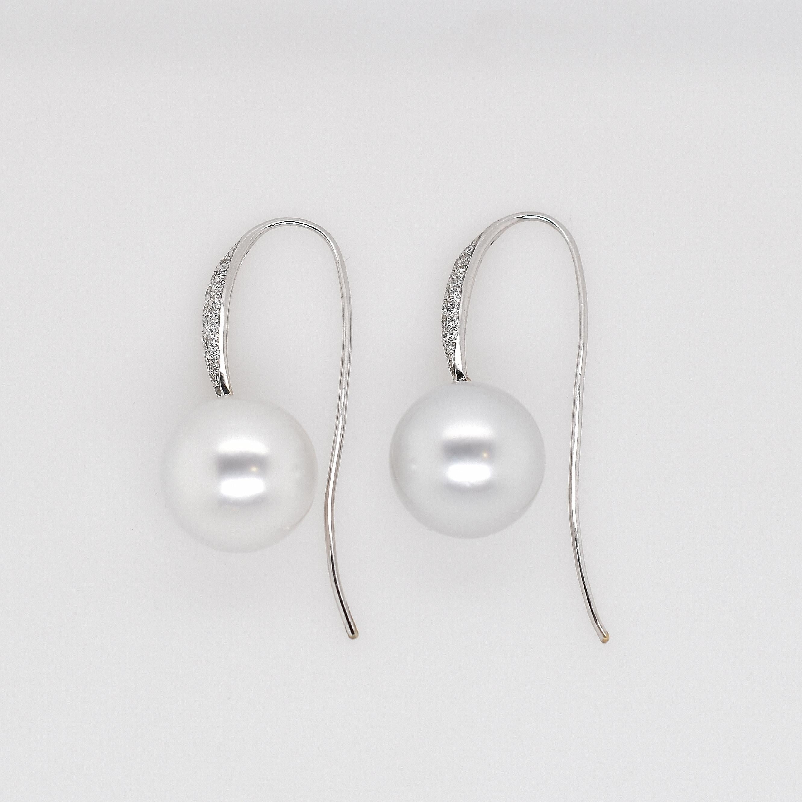 18ct white gold south sea pearl and pavé diamond drop earrings. Two 15.4mm white fine lustre south sea pearls on pavé set diamond long drop hooks. 12 round brilliant cut diamonds totalling 0.18ct and 44 round brilliant cut diamonds totalling 0.50ct