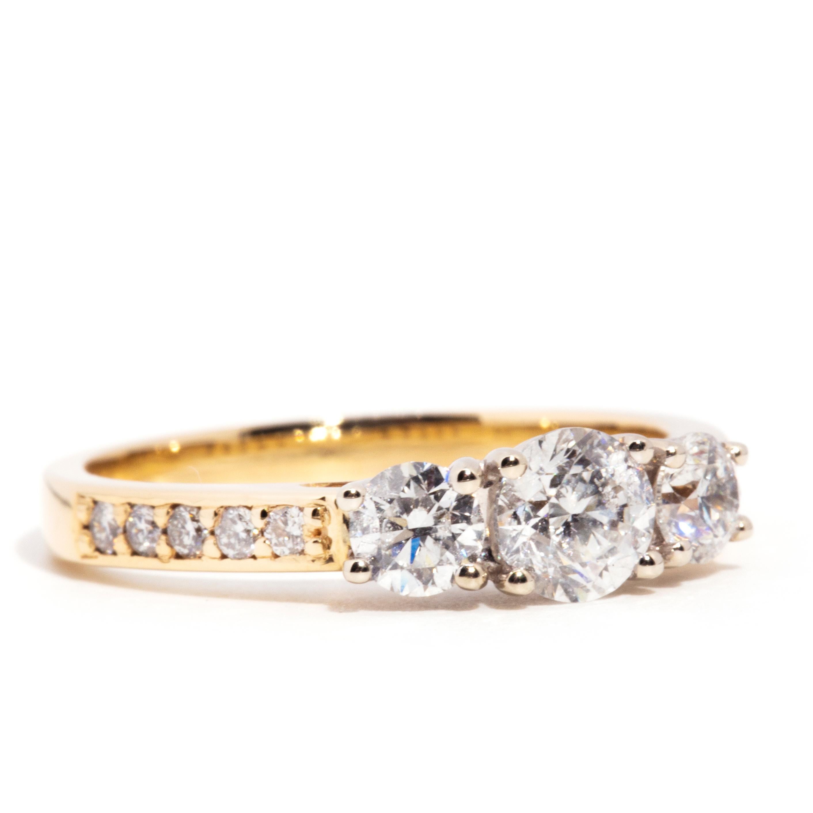 Crafted with love in 14 carat yellow gold, this captivating vintage three stone ring features an elegant band flowing into shoulders inlaid with shimmering round brilliant cut diamonds and rising into a spectacular trellis setting holding one