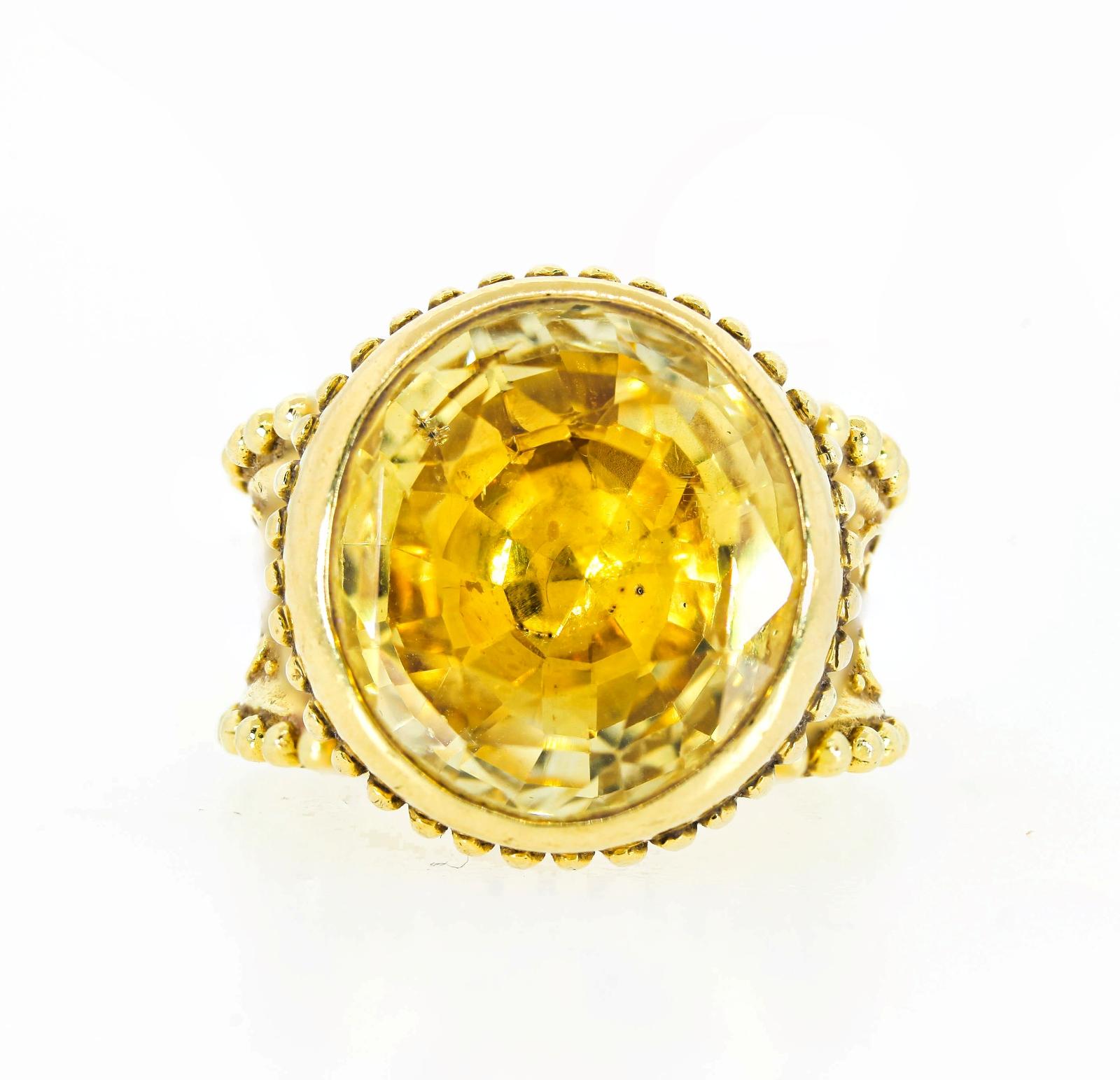 Bold and beautiful this Cynthia Bach 18KT gold ring features an oval cut Yellow Sapphire, estimated in the setting as 18.00 carat.  It is bezel set in a fluted ancient like bow cup.  The size 5 band is adorned with raised scroll work and beaded