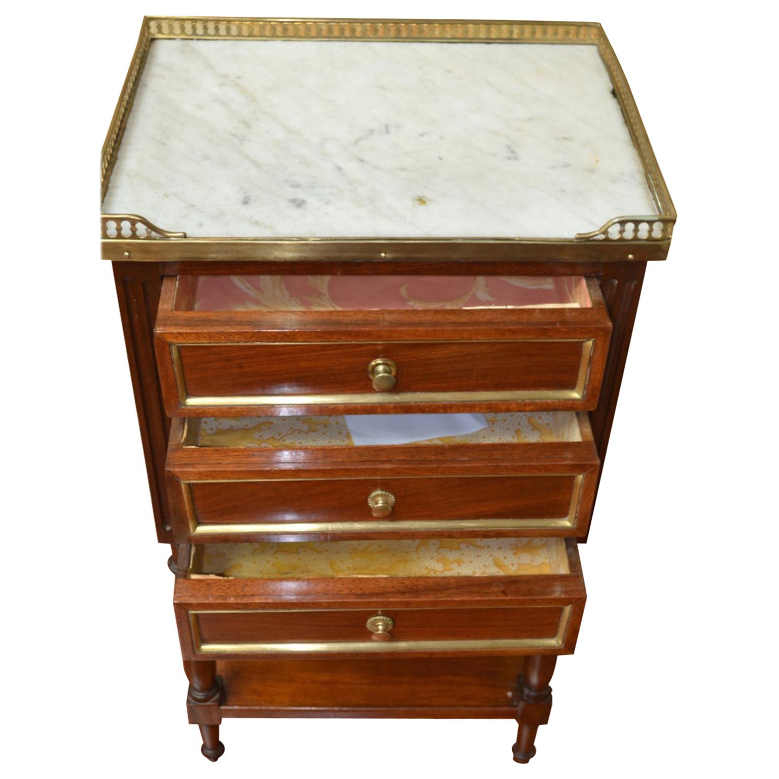 Ein Louis XVI Nachttisch auf zwei Ebenen aus gut verarbeitetem Mahagoni mit einer Platte aus weißem Marmor über drei Schubladen, die mit vergoldeten Messingfilets eingefasst sind; eine untere Ablage zwischen den vier gedrechselten Beinen.