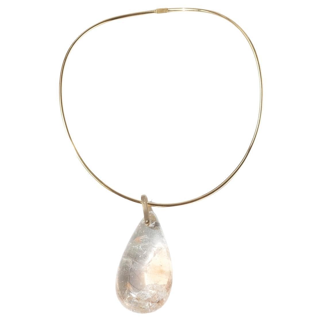 This 18 karat gold neck-ring has a large drop shaped, transparent and peach colored quartz stone with dramatic inclusions. On top of the pendant drop is a large 18 karat bail and the neck-ring closes easily with a screw lock. The neck-ring can of