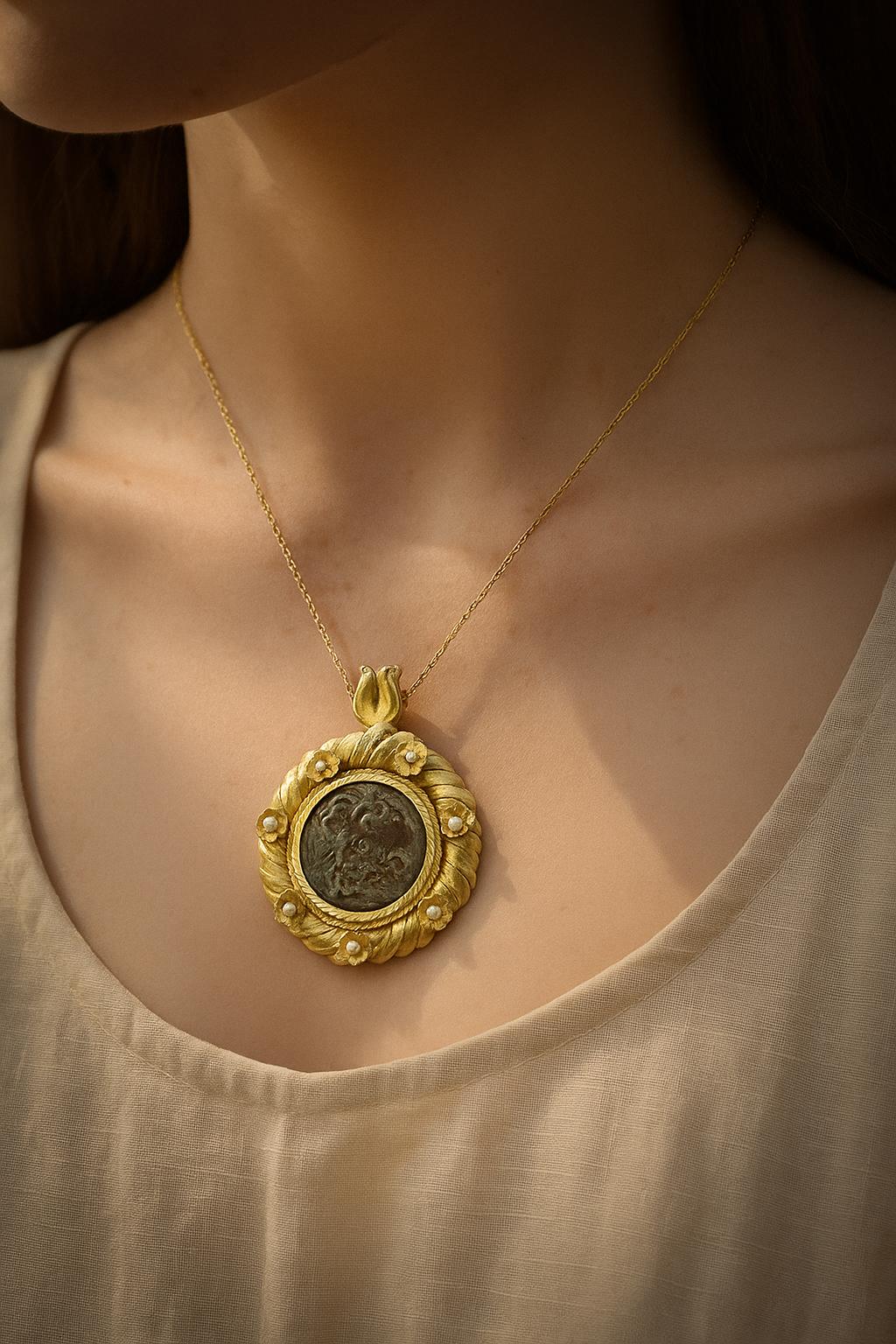 Marque et modèle : Pendentif orné, or jaune 18 carats, présentant une véritable pièce de bronze ptolémaïque

Poids : 64 g

Diamètre : 5,5 cm
Perles : 7 perles de culture rondes, ~4 mm chacune
Pendentif poinçonné 750 et marque du fabricant.

Travail
