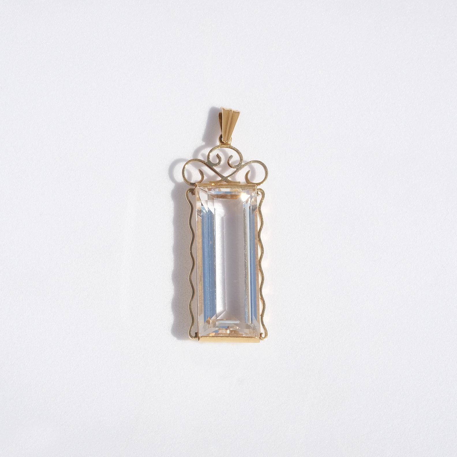 This 18 karat gold pendant has a faceted baguette cut rock crystal which is embraced by a beautiful pattern resembling a royal monogram. 

The pendant shows upon elegance and it fits well in both an everyday environment as well as in a more festive