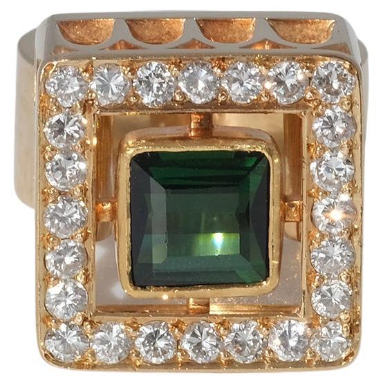 Dieser Ring aus 18 Karat Gold hat einen Turmalin und 24 Diamanten im Brillantschliff. Der Kopf des Rings hat eine quadratische Form mit einem Muster, das an die Fensterrahmen einer alten englischen gotischen Kathedrale erinnert. 

Der Ring strahlt