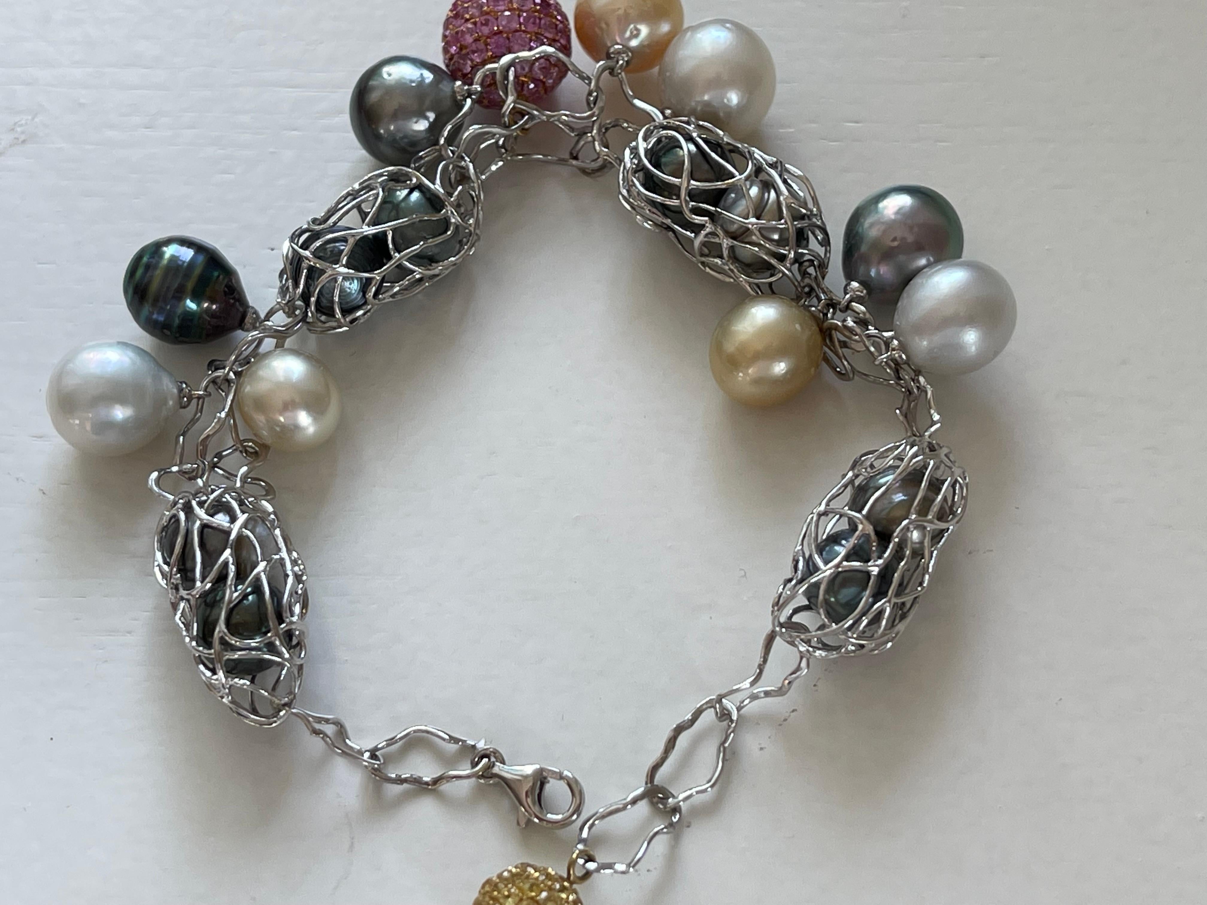 This delicate, stylish charm style bracelet is fashioned from 18 K white Gold interlocking wire circles featuring 6 golden and white South Sea Pearls pearls and 11 Tahitian Pearls and 2 balls all pavé set with yellow and pink Sapphires weihging 6.50