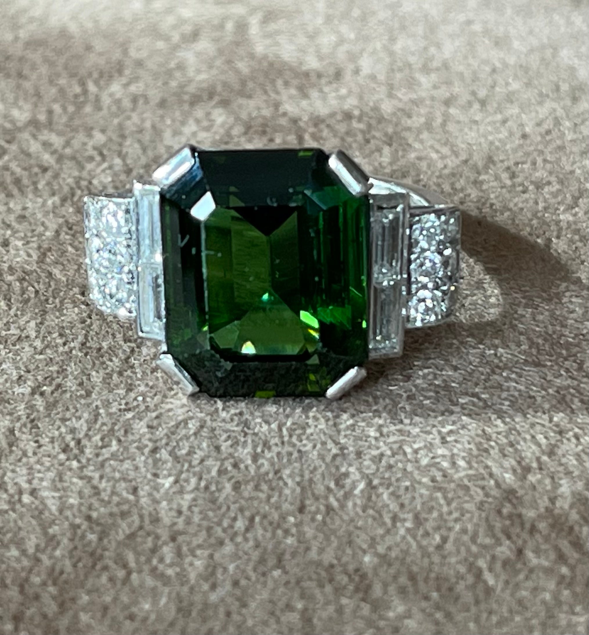 This classy tourmaline and diamond statement ring is crafted in solid 18-karat white gold, weighing 7.34 grams. Displaying a prominent prong-set, rectangular tourmaline of deep green color, weighing approximately 6 carats, flanked by 2 baguette