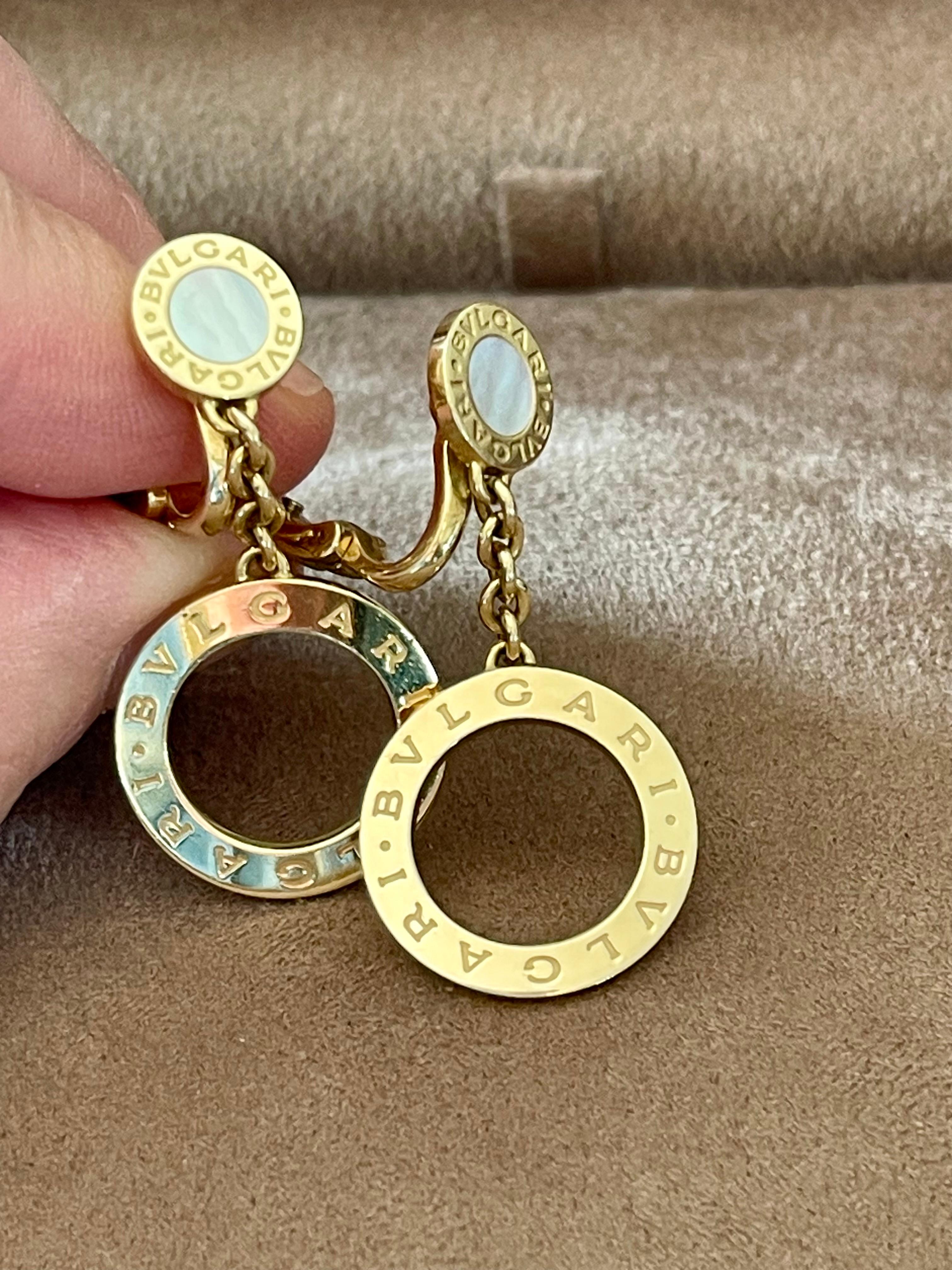 These are authentic BULGARI 18 K Yellow Gold Mother Of Pearl BVLGARI BVLGARI Drop Earrings. These stylish clip on earrings feature a mother of pearl encircled by the BVLGARI name logo on a flat disk of 18 Karat yellow Gold with a an cutout disk