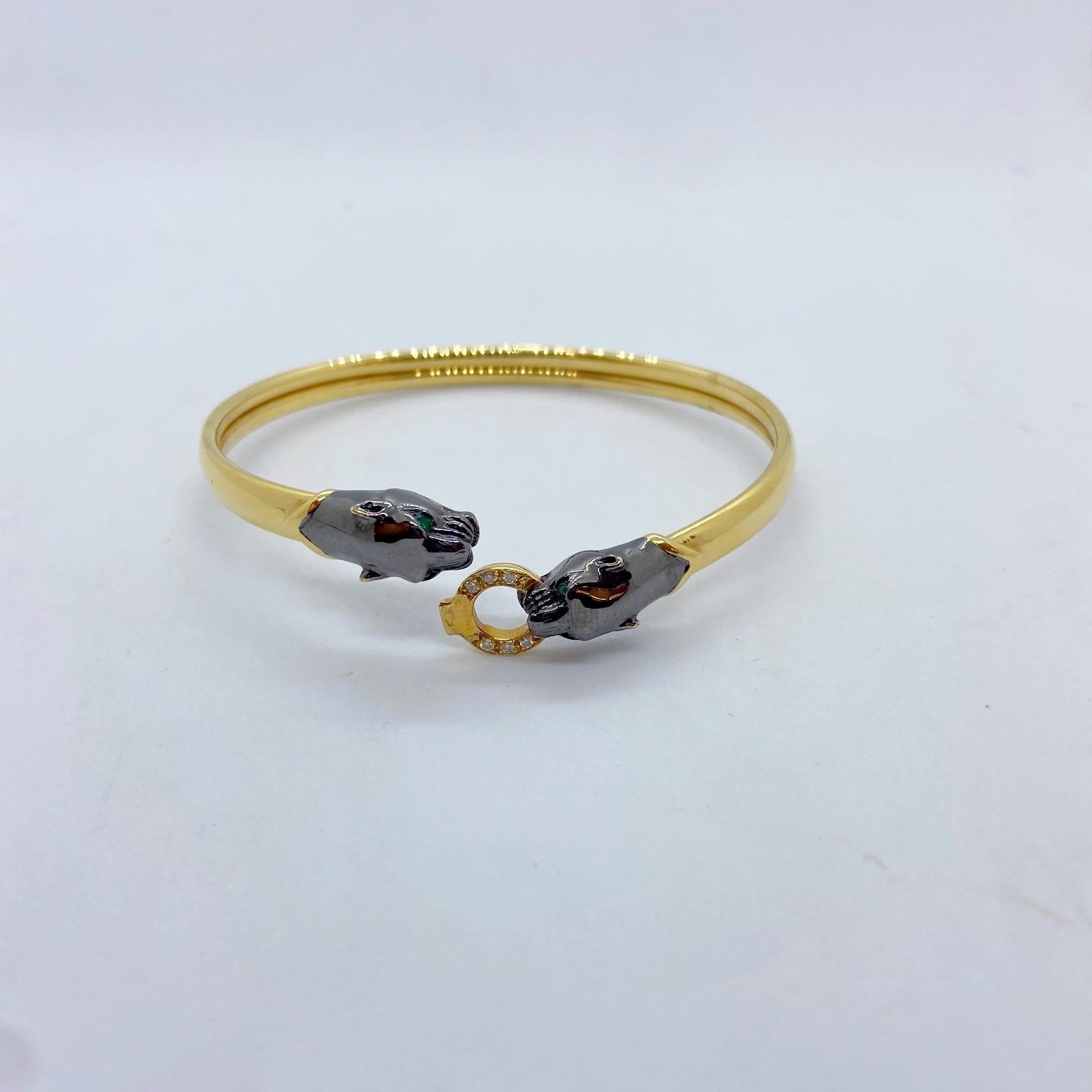 The bracelet is designed in 18 karat yellow gold with two blackened gold Panther heads. Each Panther has Emerald eyes. They hold a ring set with round brilliant Diamonds in their mouths. the bracelet unlocks at the top when the ring and mouth are