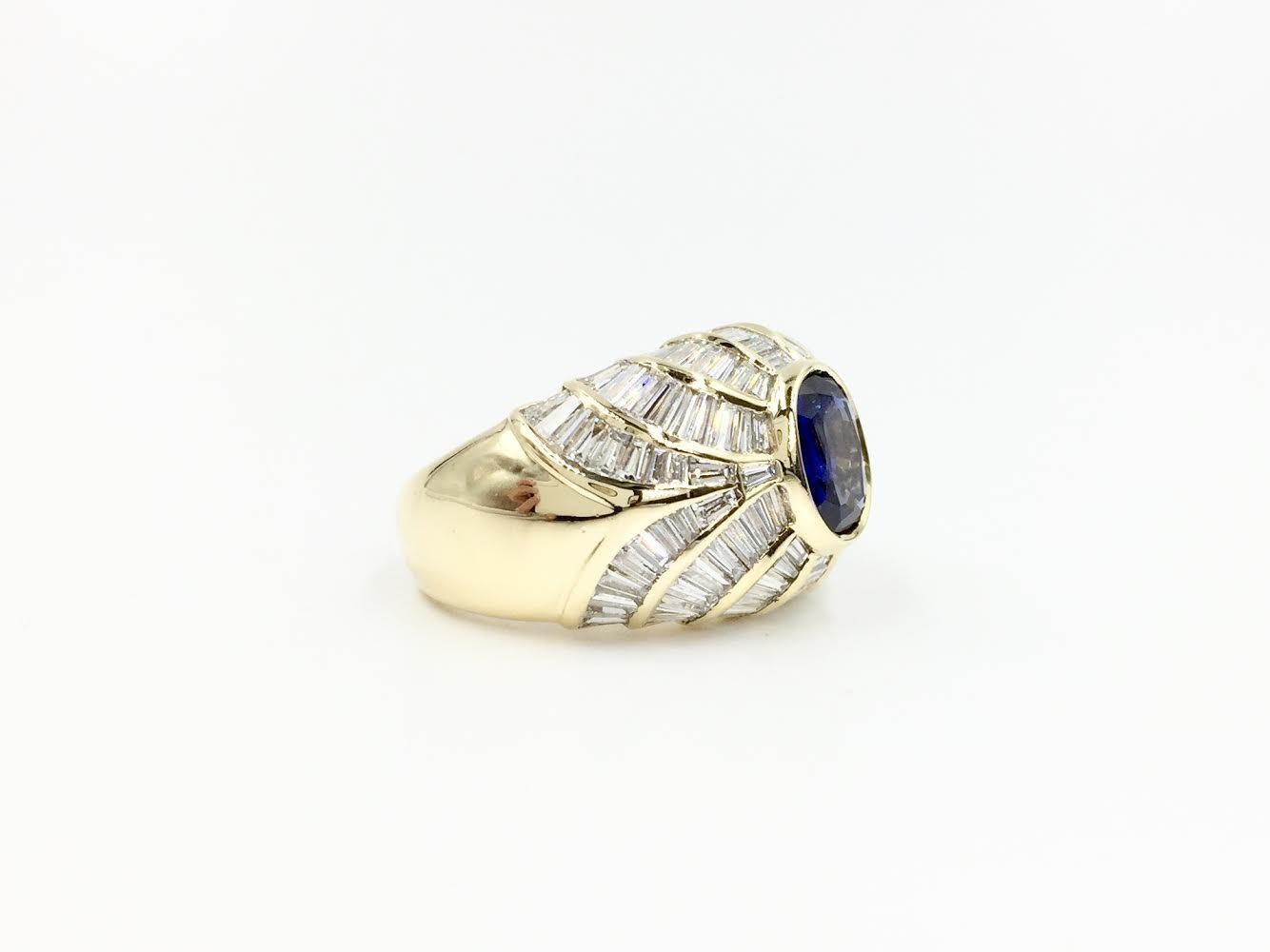 A fabulous find! This Art Deco inspired 18 karat yellow gold domed cocktail ring features 3.43 carats of beautiful baguette diamonds, perfectly channel set in a unique pattern across the top of the ring and a gorgeous bezel set oval blue sapphire
