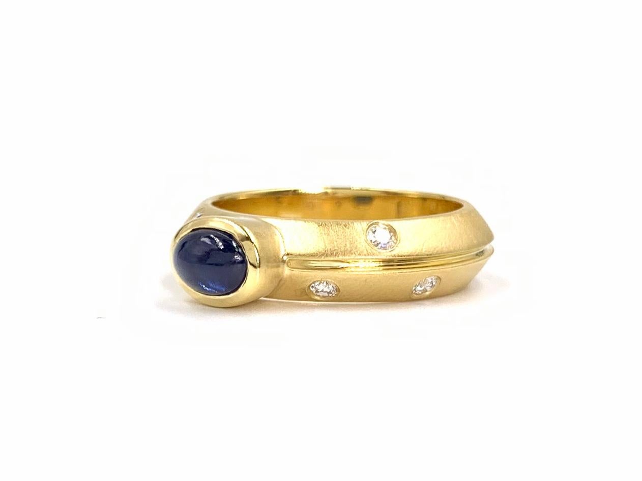 A wearable and beautifully satin finished 18 karat yellow gold 5mm ring featuring a bezel set .74 carat cabochon blue sapphire and 6 round brilliant burnished diamonds at .12 carats total weight. Diamond quality is approximately F color, VS2