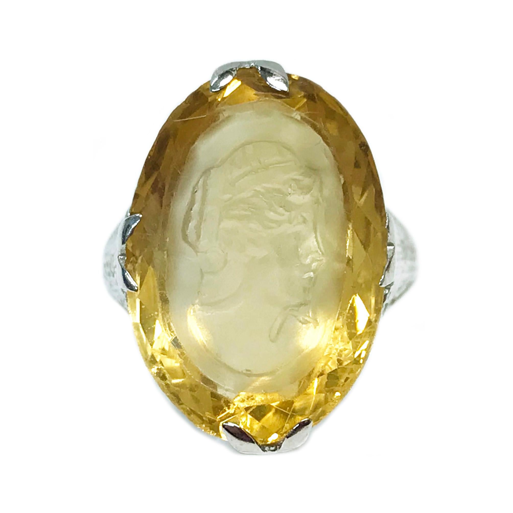 18 Karat White Gold Citrine Intaglio/Relief Ring. The ring features an oval 17mm x 12mm light Citrine stone with the image of a Roman female head in relief. The thin-band has an Art Deco filigree motif toward the top and a smooth shiny finish band.