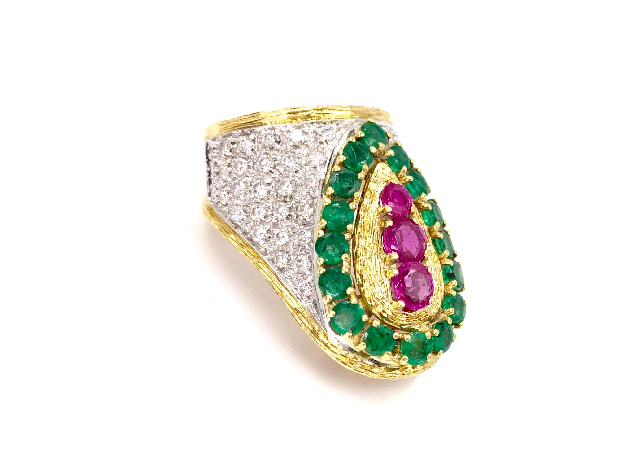 A truly unique find. This large 18 karat two tone gold diamond, emerald and ruby ring has an eye-catching curvy shape and design, made to rest upon the knuckle. Ring features three vibrant rubies at approximately 1.75 carats total weight. Sixteen