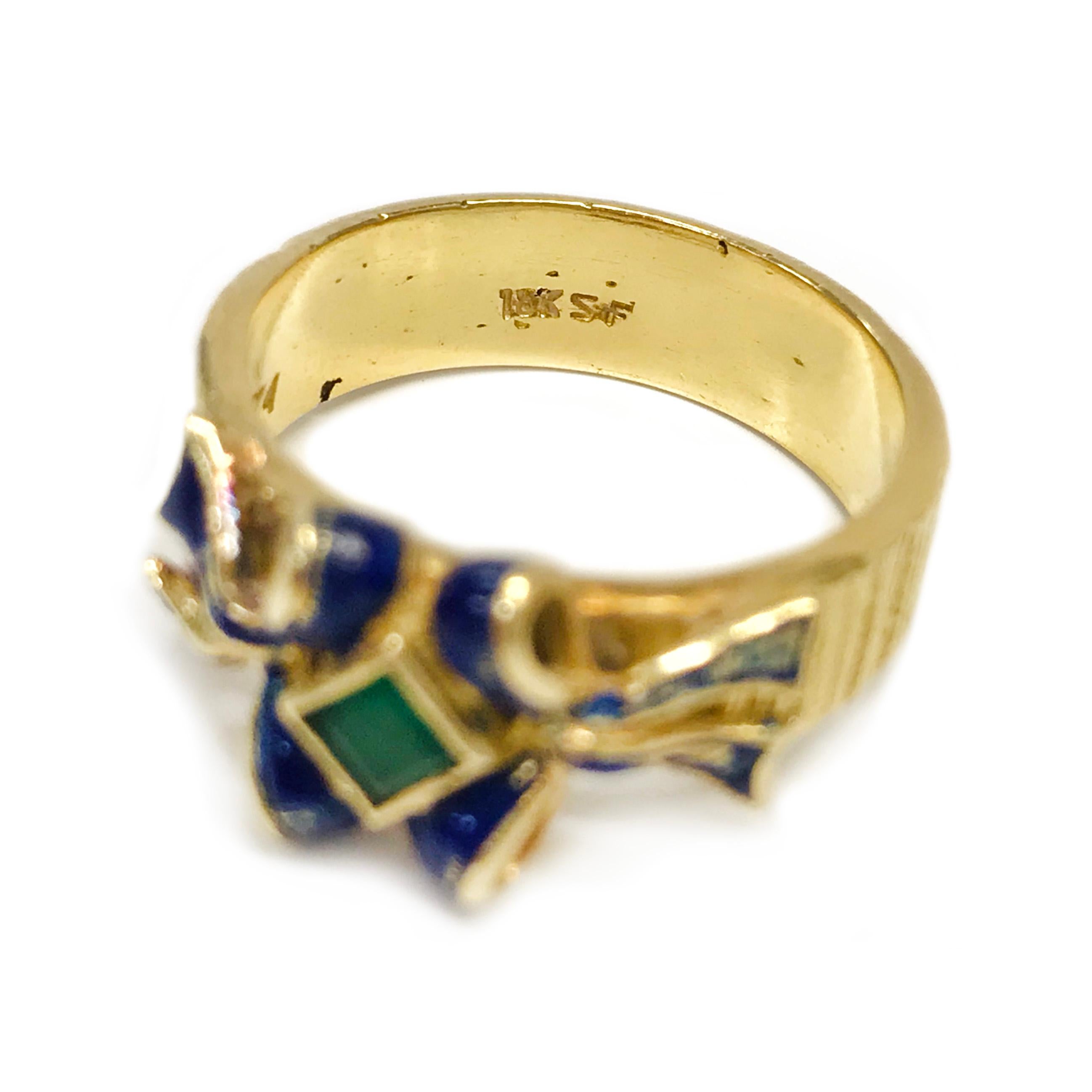 18 Karat Emerald Enamel Ring. The ring features a single square-cut Emerald with side bows accented with blue enamel. The ring band is highly textured with vertical lines. The ring is 22.3mm tall x 19.2mm wide x 8.9mm deep. The ring size is 6.