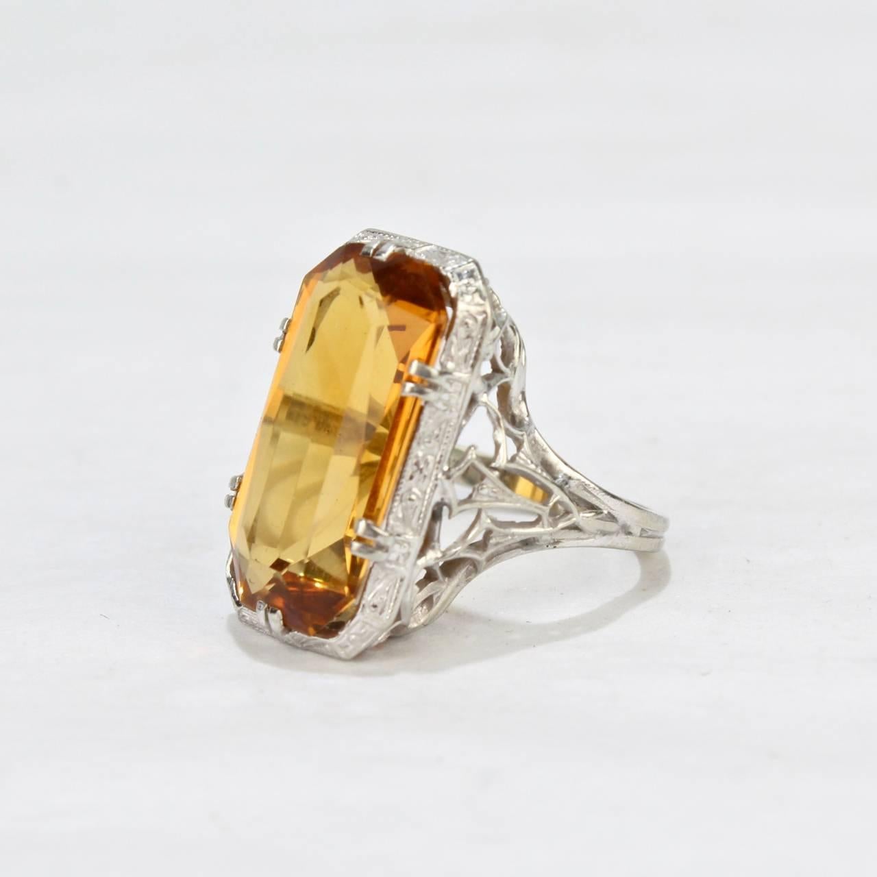 A fine emerald-cut Citrine cocktail ring 

With an Art Deco style 18-karat white gold filigree setting

The shank is stamped MG 18K

Ring size: ca. size 4
Stone length: just over 2/3 in.
Stone width: ca. just over 1/3 in.
