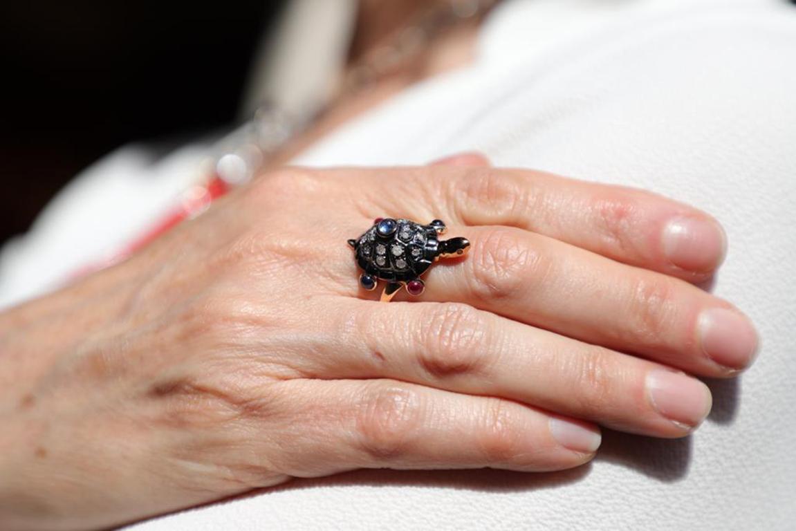 Rossella Ugolini Design collection, a Turtle shaped cocktail ring handcrafted in 18 Karats Rose Gold and adorned with 6,40 Karats Cabochon Sapphires, 0,60 Cabochon Ruby, 0,35 Grey Diamonds. 
The eyes and the tail are set with little diamonds