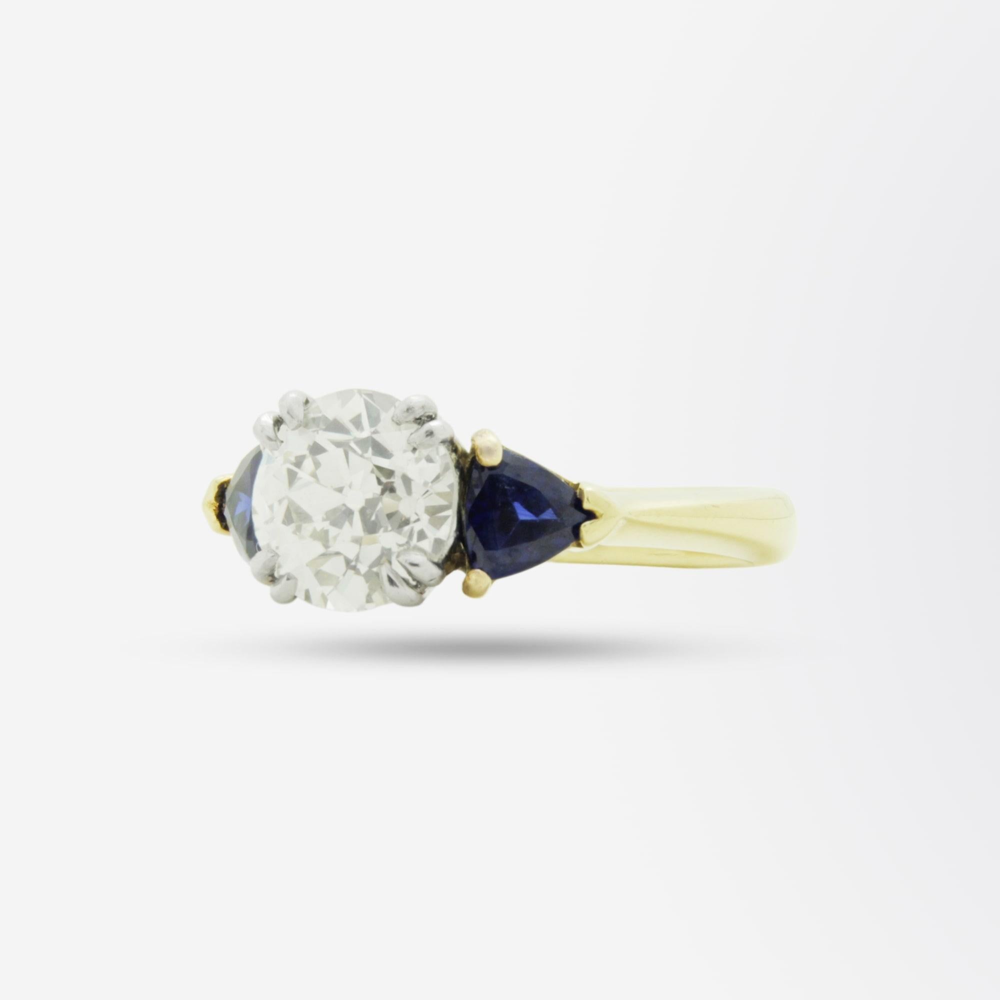 An 18 karat gold, diamond, and sapphire ring featuring a central old European cut diamond weighing 2.15 carat. The diamond is flanked by a pair of trillion cut sapphires, totalling 1 carat, which add to the beauty of this simple, yet elegant ring.