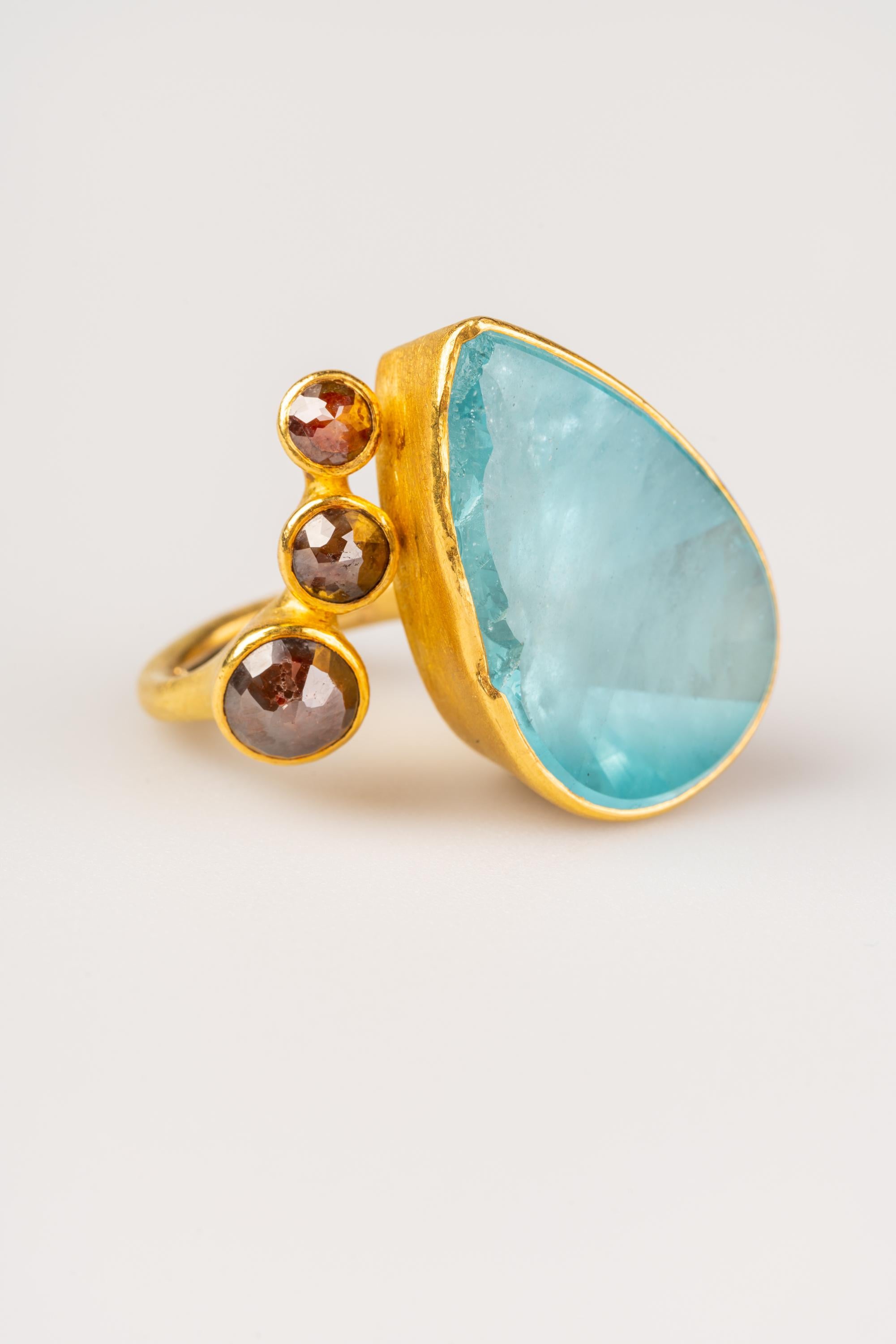An 18k yellow gold ring set with a pear shaped natural surface aquamarine, 45.82 carats and 3 rose cut reddish brown opaque diamonds for a total of 3.23 carats. Ring size 8. This ring was designed and made by Peter Schmid.