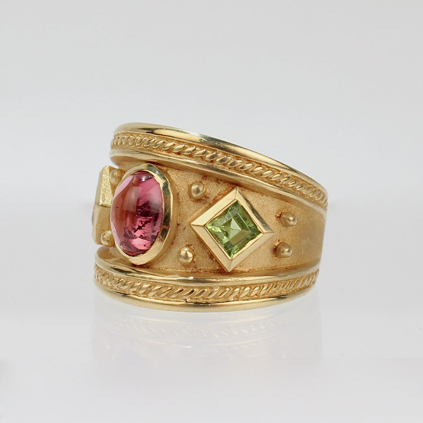 A very fine 18 karat gold and multi-gemstone cocktail ring in the Etruscan style.

The wide band ring is constructed of both polished and matte finished golds and has a bezel set oval amethyst cabochon gemstone at the center. 

The amethyst is