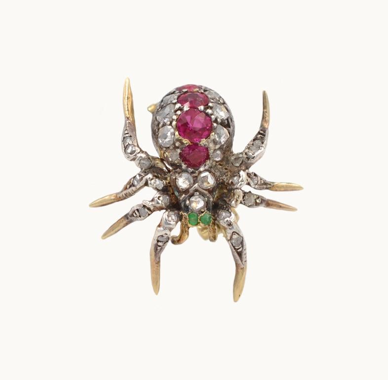 Antique Victorian spider brooch in 18 karat yellow gold and silver from circa 1890s-1900s.  This incredible spider features 29 rose cut diamonds, 4 rubies, and 2 emeralds. 
This brooch measures approximately 0.86 inches in length, 0.83 inches in
