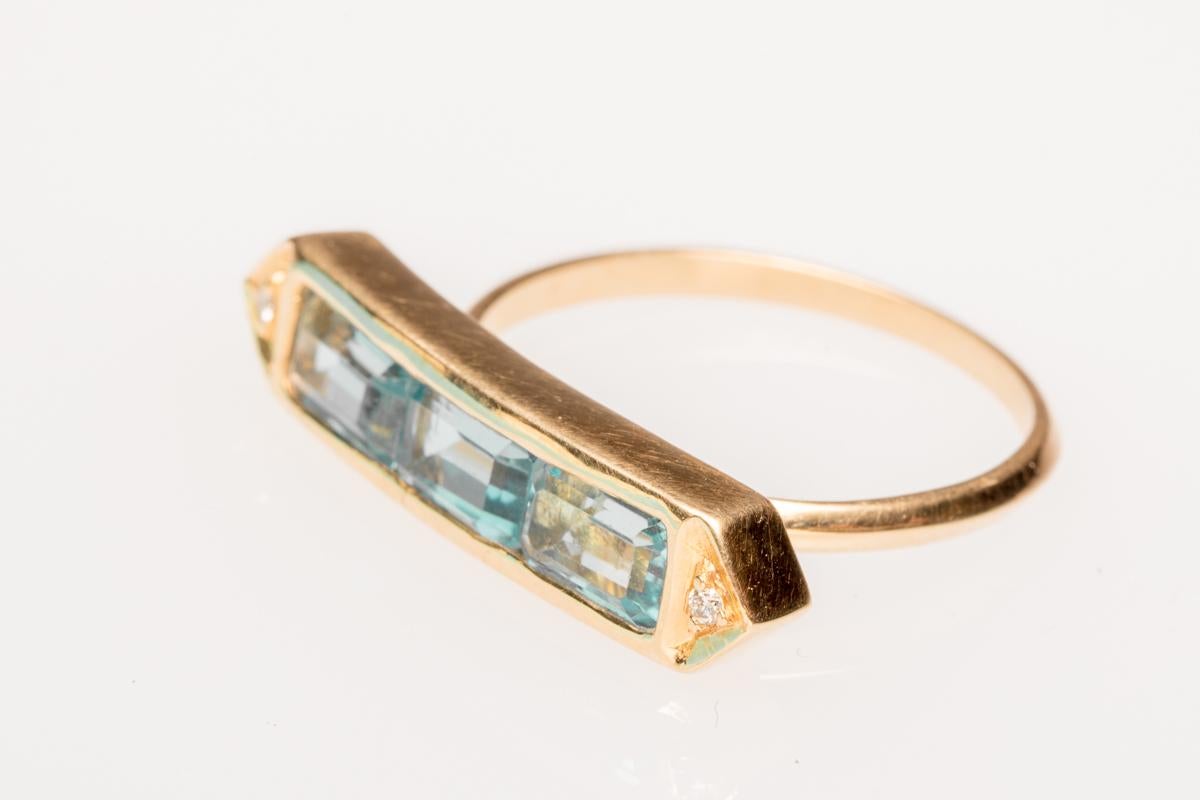 Three emerald cut aquamarines in an 18K gold setting.  Faceted diamonds on each corner.    Carat weight of aquamarines is 3.14.  Ring size is 6.75.