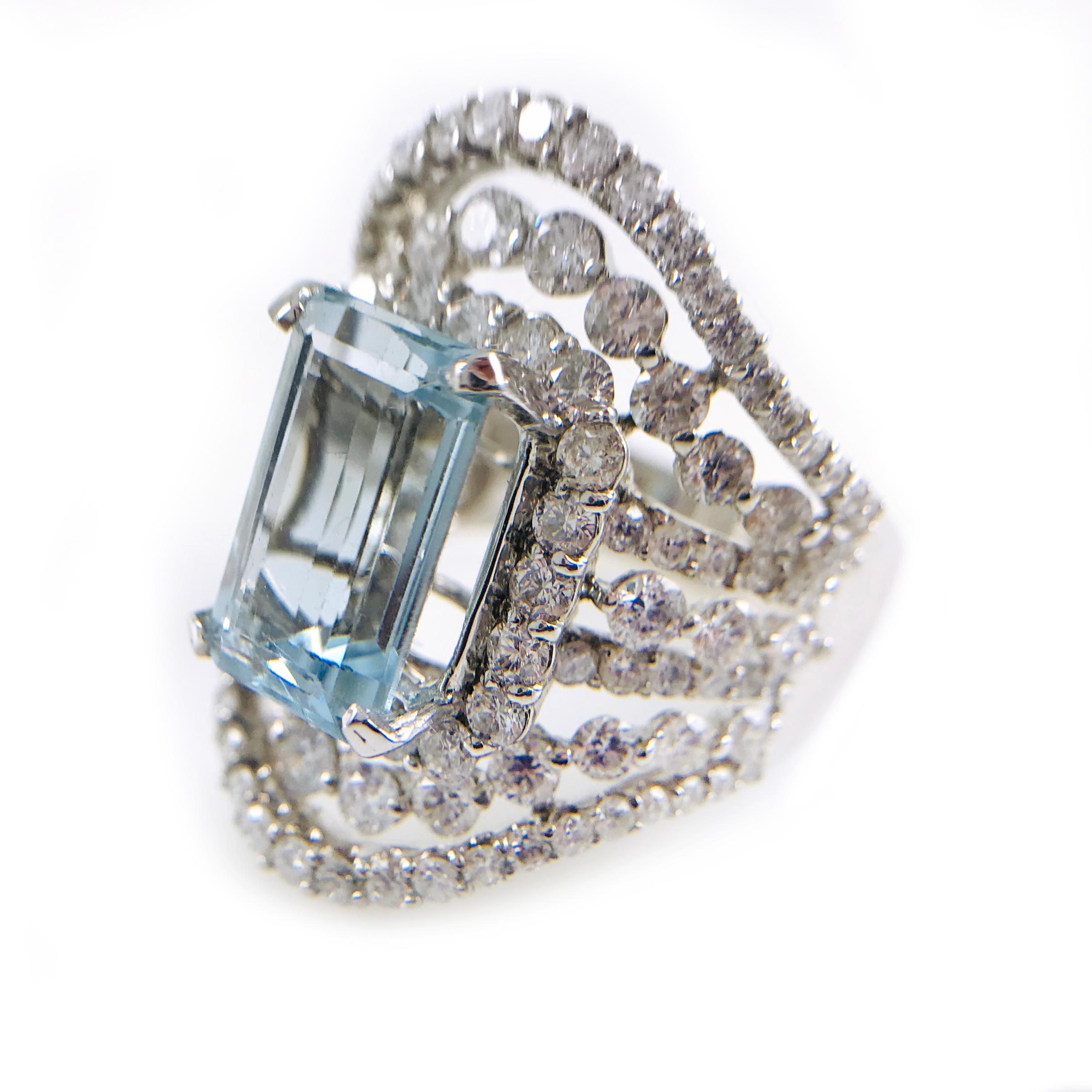 18 Karat Gold Cigar-shaped band with a Step-Cut Aquamarine prong-set in the center. The Aquamarine measures 13.2 x 7.5 x 5.2mm and has a carat weight is 6.5 ct. Multiple rows of round prong-set diamonds surround the center gemstone. The diamonds are