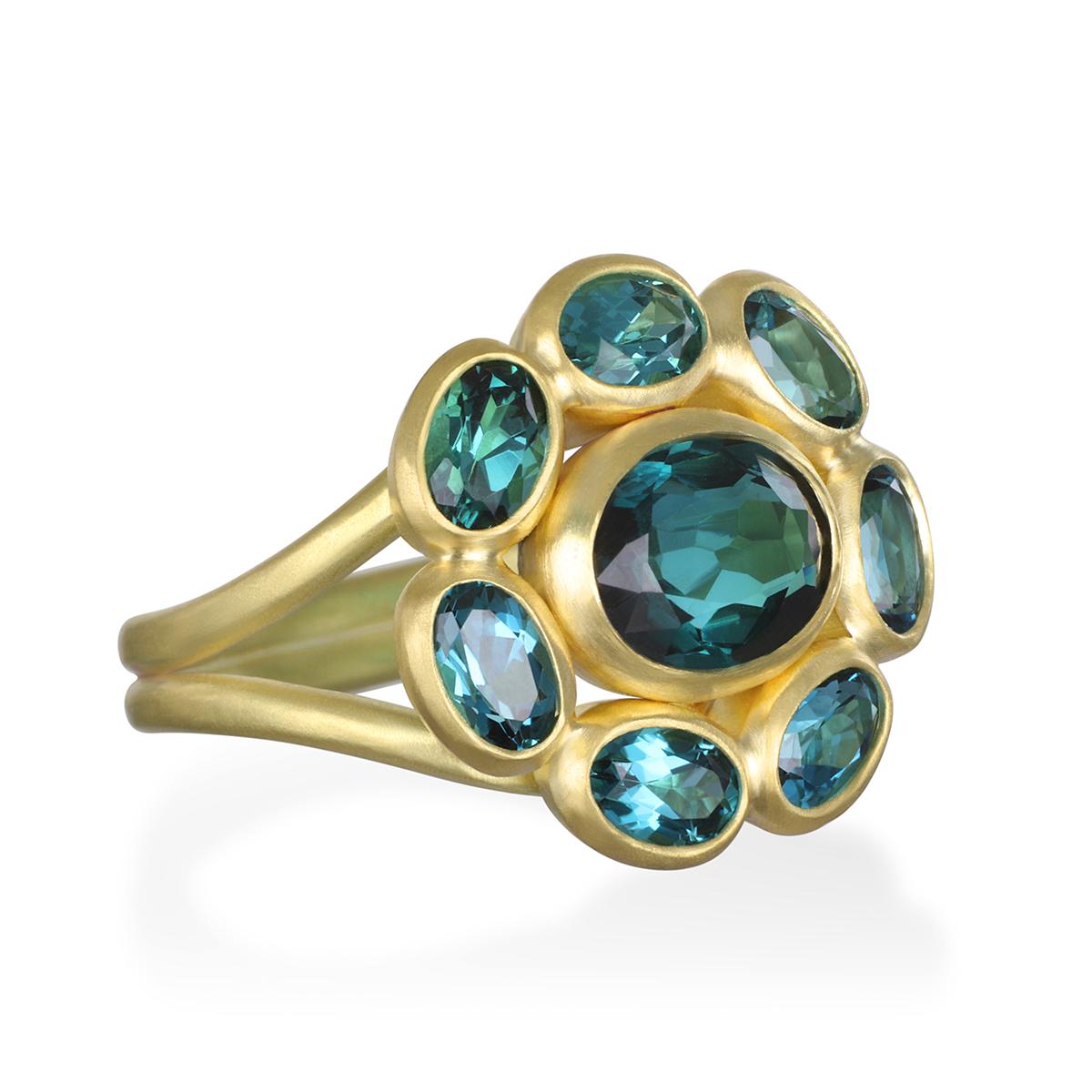 Faye Kim's handcrafted 18 Karat Gold Blue-Green Tourmaline Daisy Ring, with its bezel settings and matte finish, marries nature's beautiful blue greens with the timelessness of gold to create a work of art. The spectacular faceted oval Tourmaline