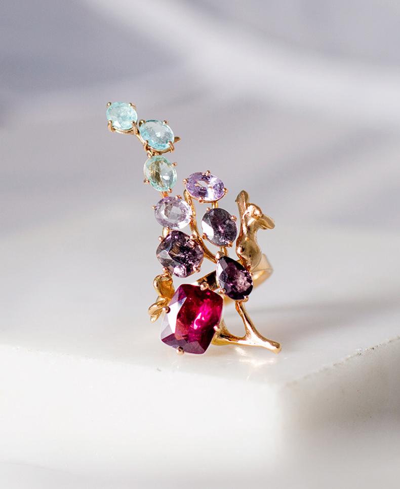 This 18 karat yellow gold contemporary cocktail cluster ring is a true art object due to its unusual form and encrusted gems: fancy pink and green sapphires, Paraiba tourmalines, and spinel, totaling 14.36 carats.
This piece can be personally