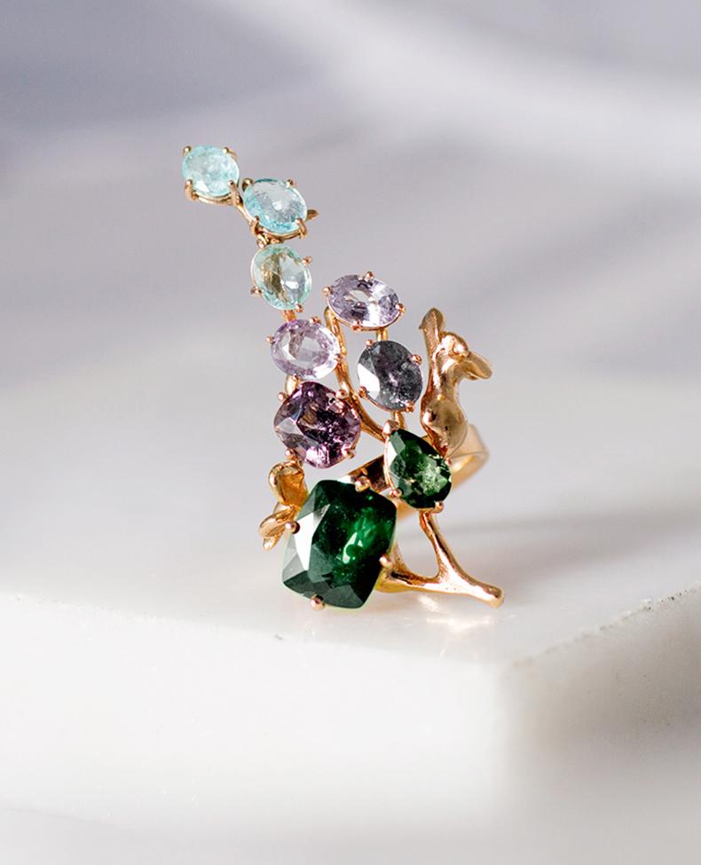 This 18 karat rose gold contemporary cocktail ring is an art object with its unusual form. It is encrusted with 12 carats of rose and green sapphires, Paraiba tourmalines, and spinel.

The workmanship is precise, and the piece sparkles as the